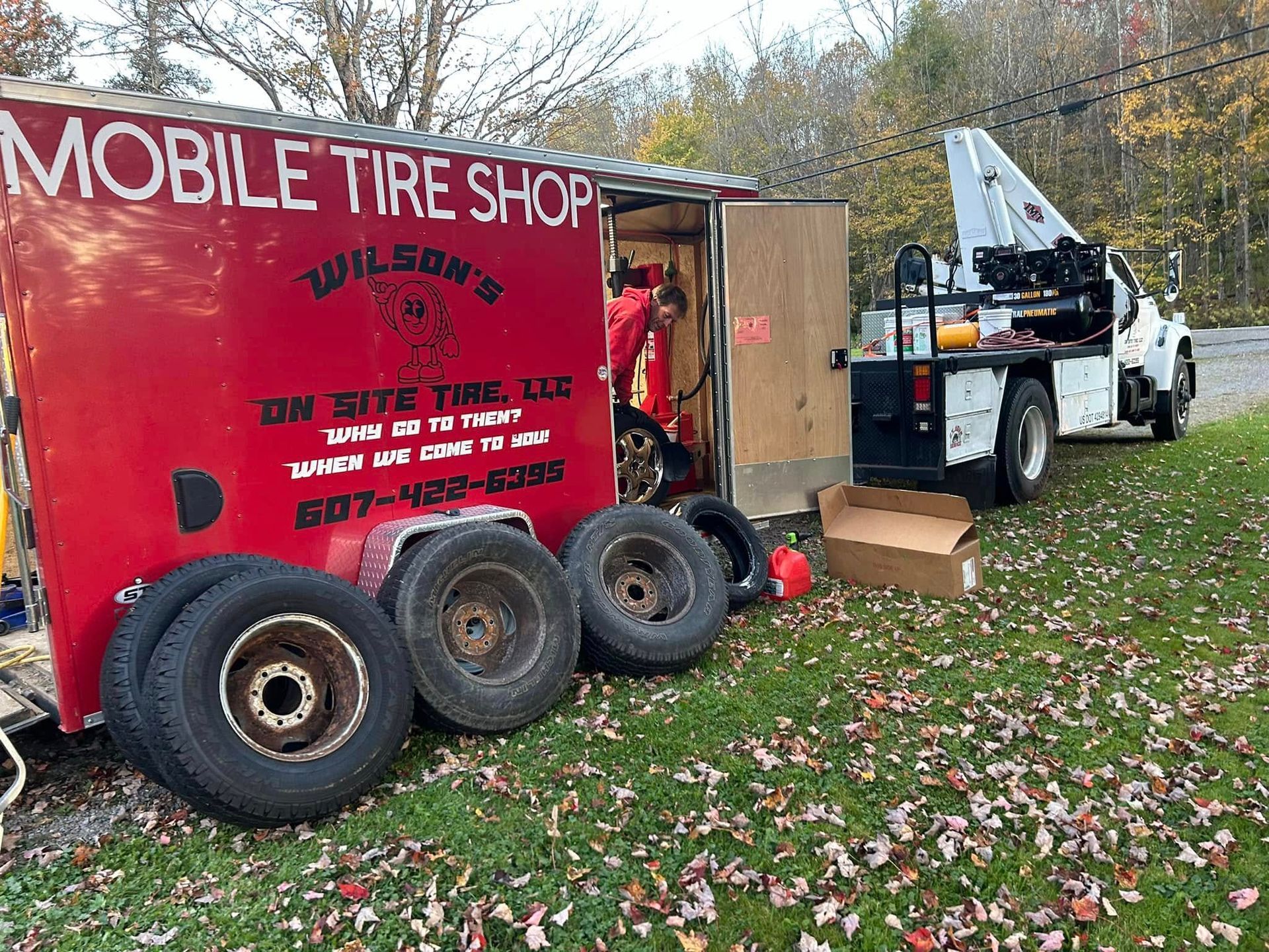 A mobile tire shop trailer is parked in the grass next to a truck.
