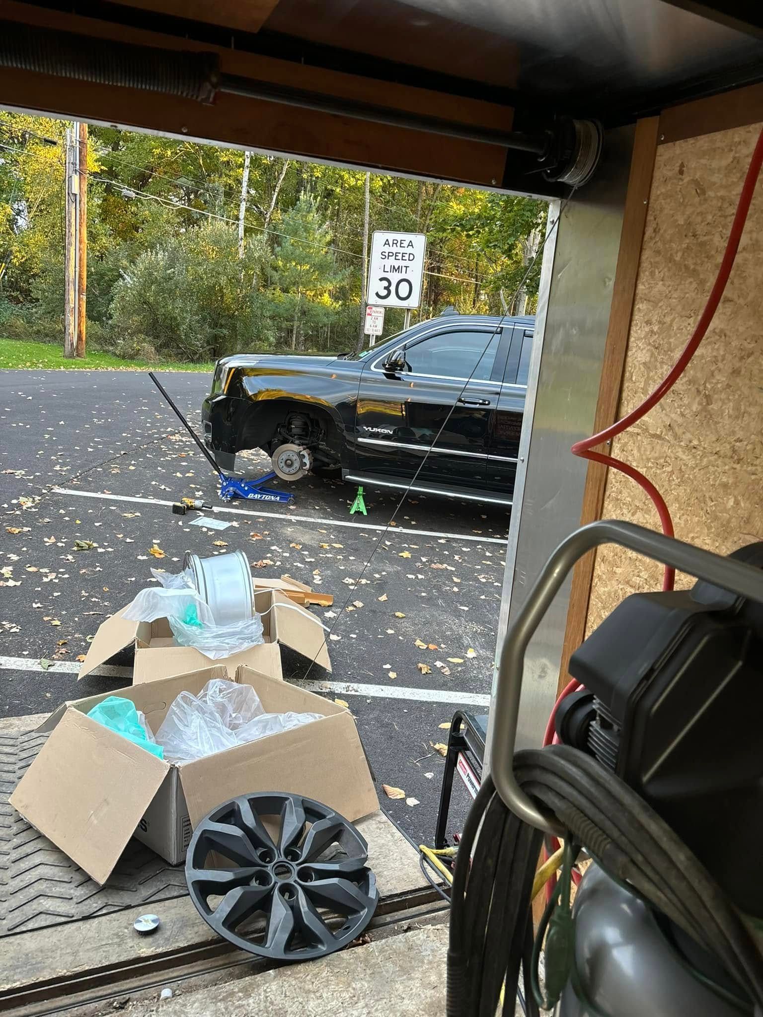 A car is parked in a garage next to a box of wheels.