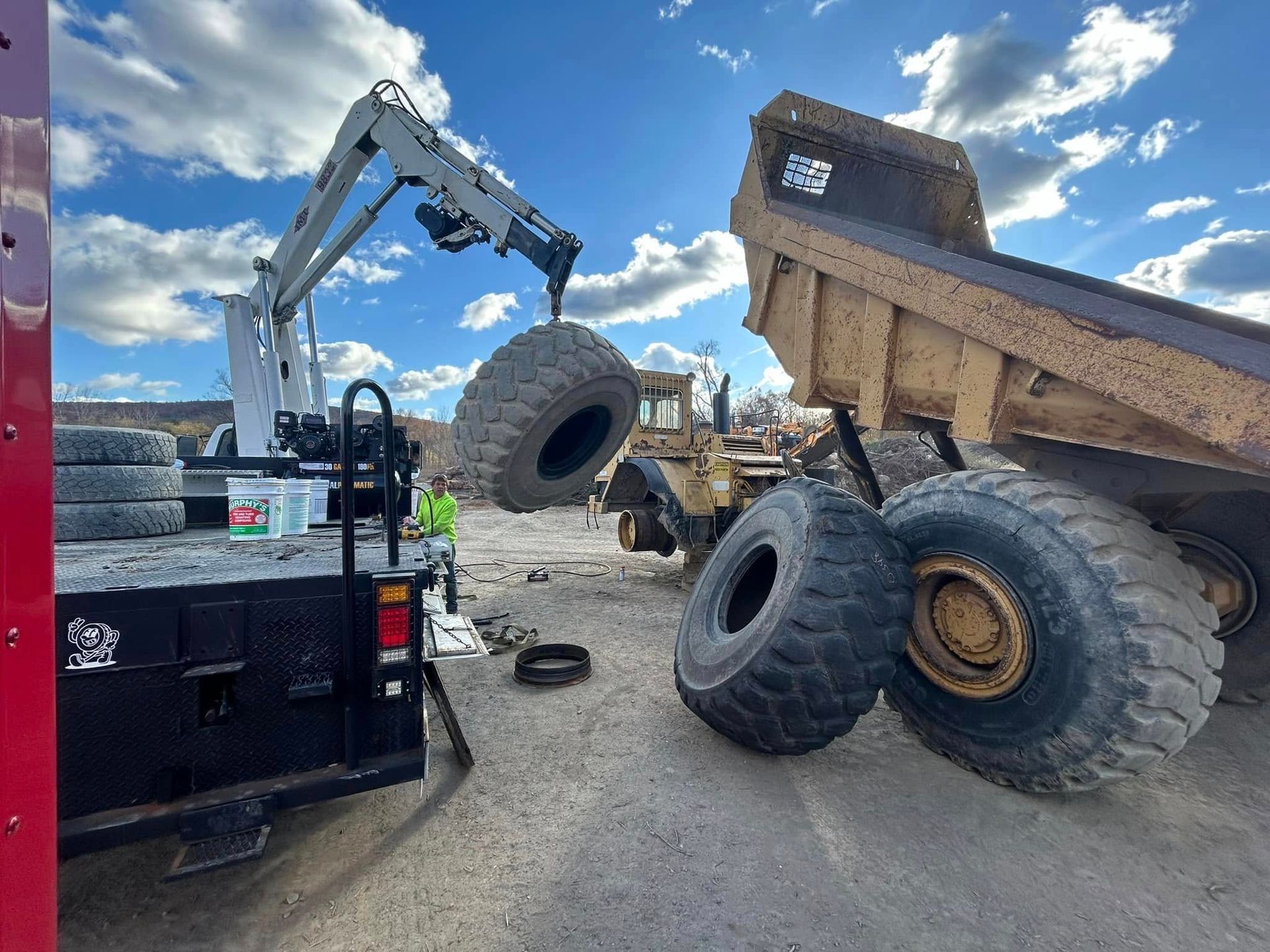 A crane is lifting a tire from a dump truck.