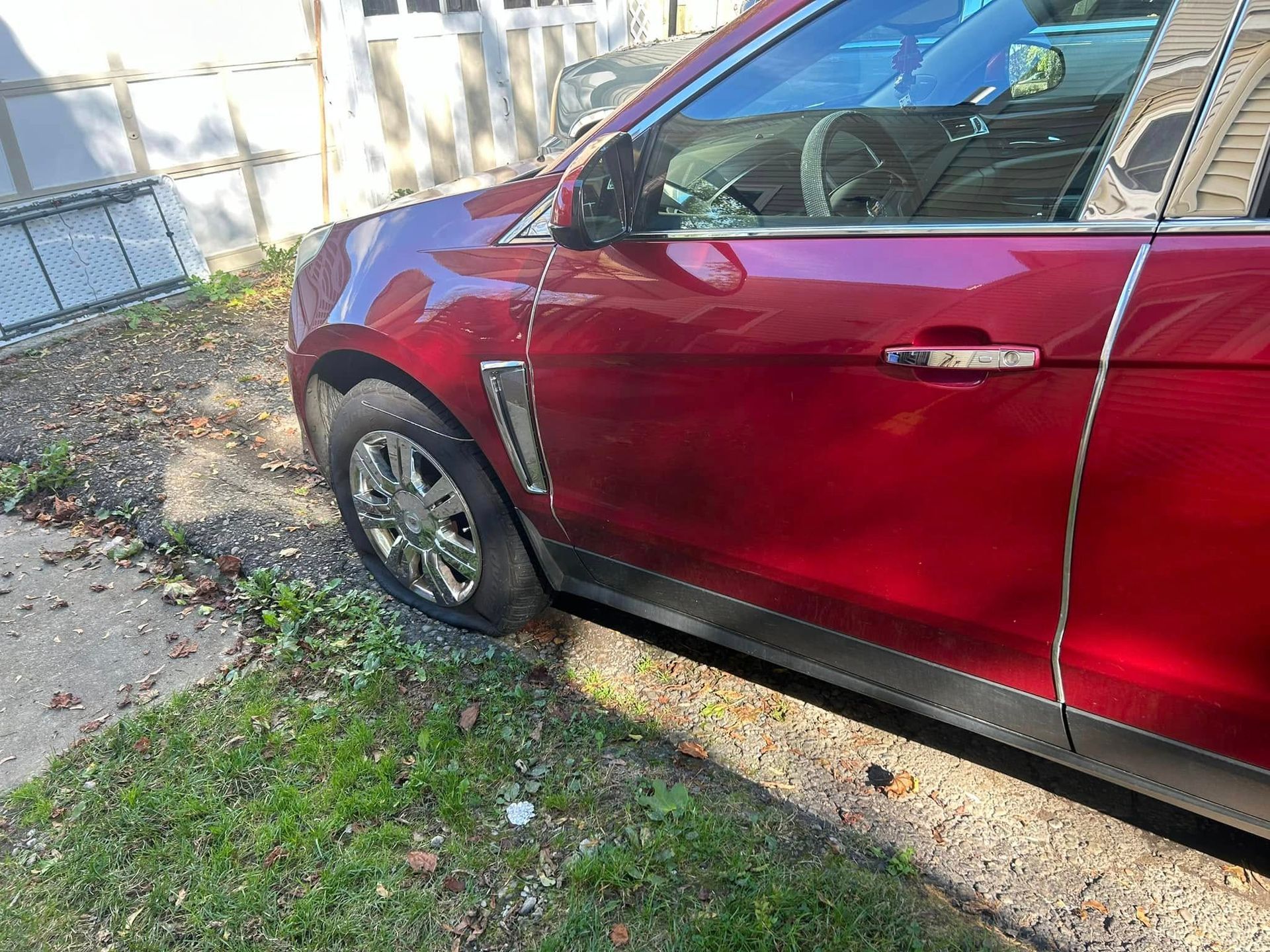 A red car is parked in a driveway next to a house.