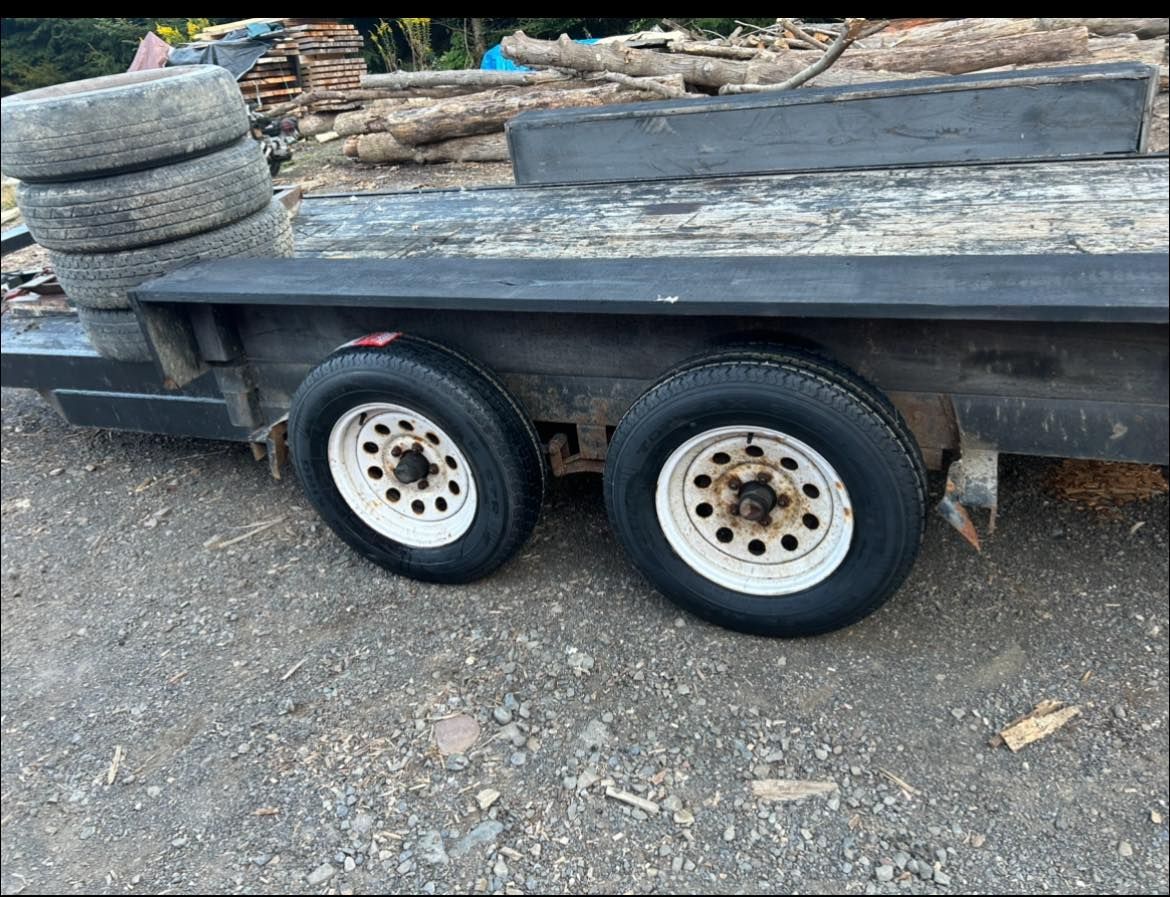 A trailer with tires and logs on it is parked on the ground.
