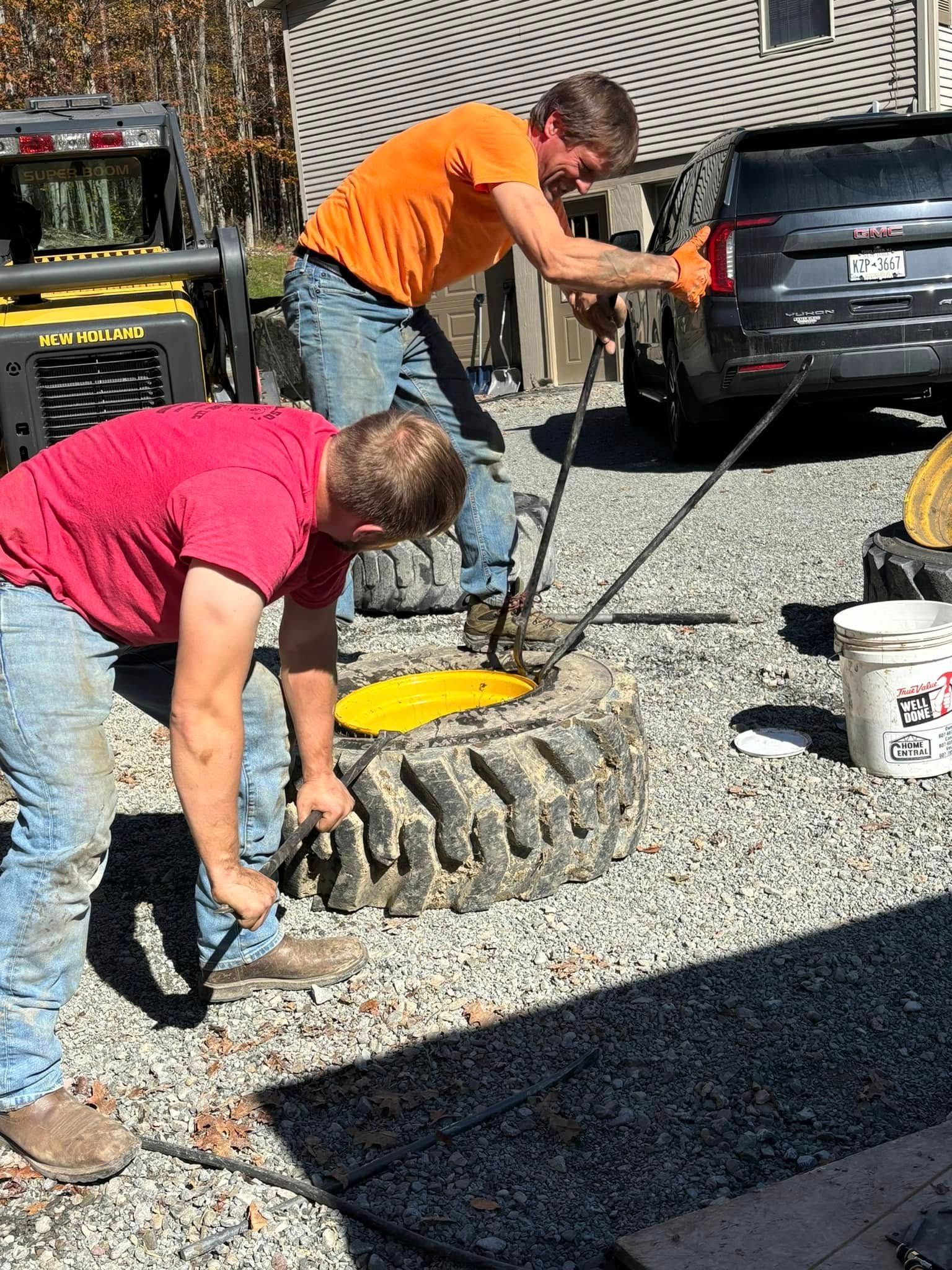 Two men are working on a tire in a gravel driveway.