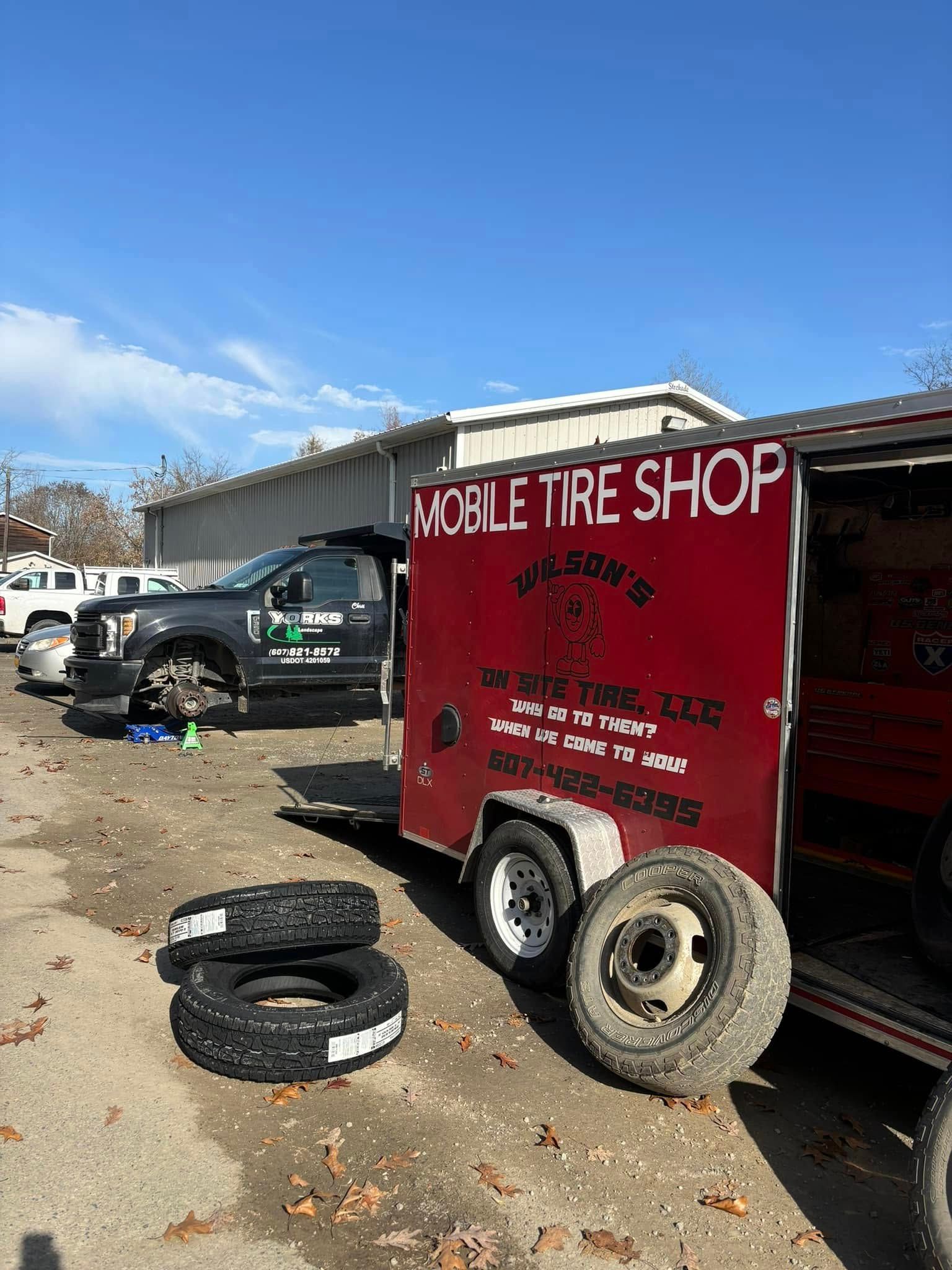 A red trailer with tires on it is parked in front of a tire shop.