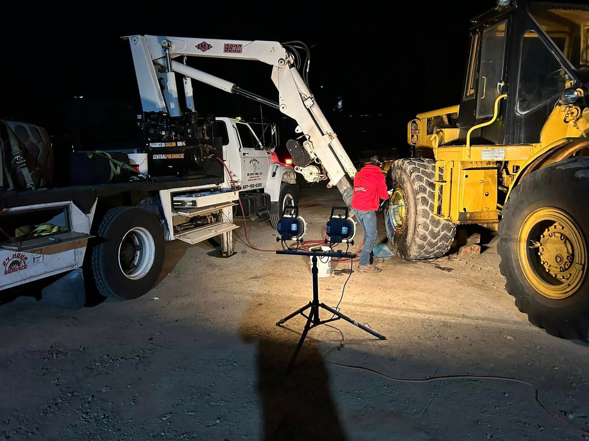 A man is working on a tractor at night in a parking lot.