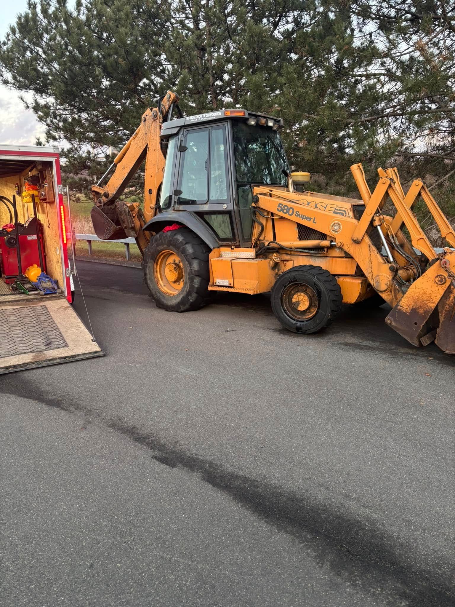 A yellow backhoe is parked on the side of the road next to a truck.