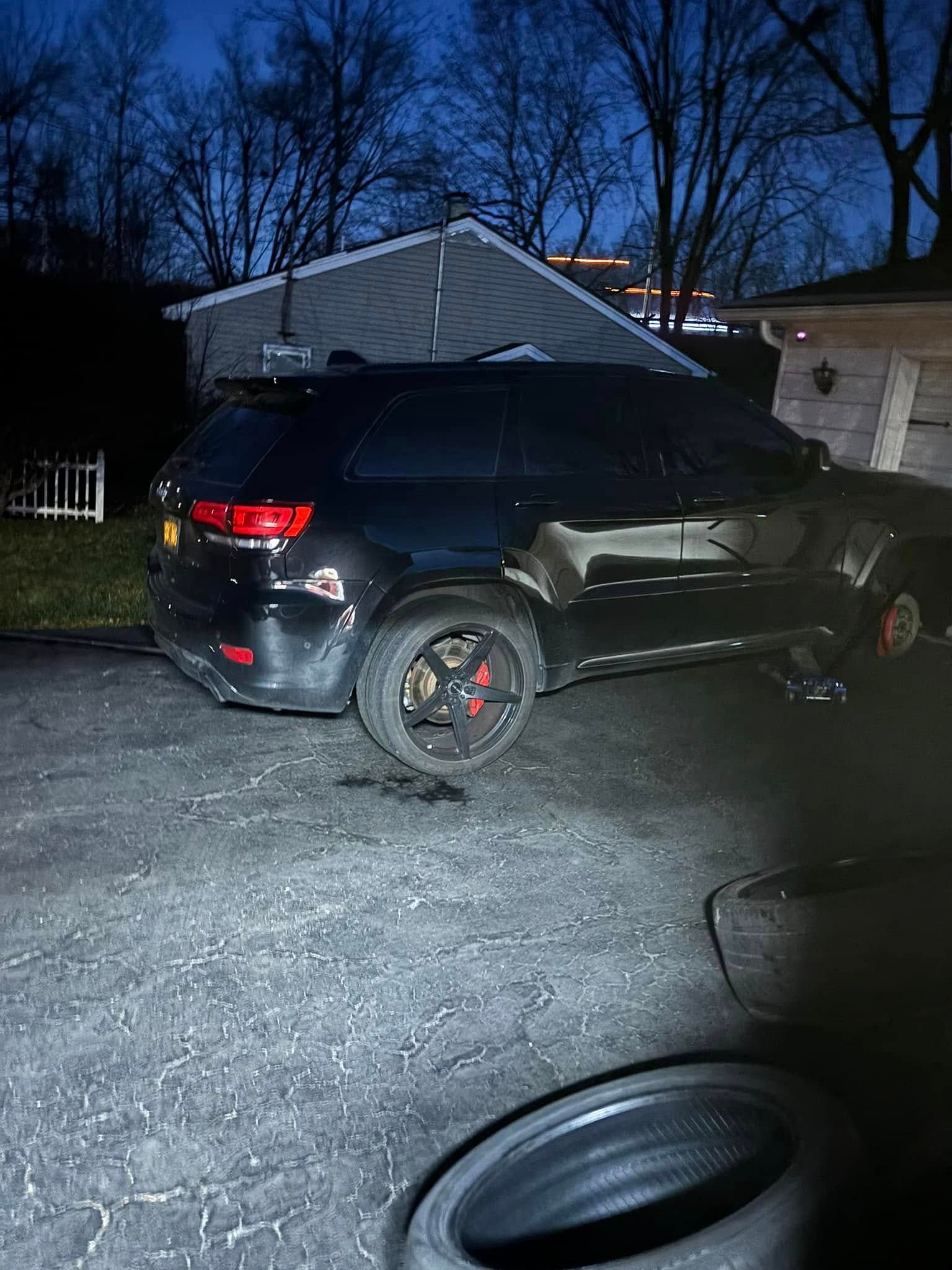 A black suv is parked in a driveway next to a pile of tires.