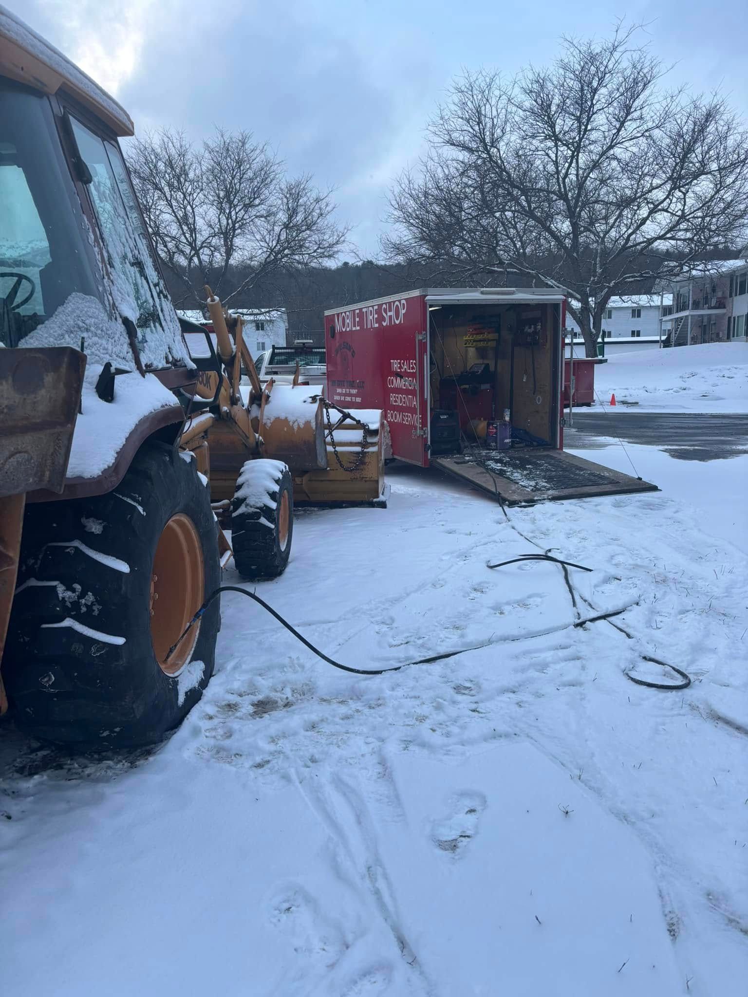 A tractor is sitting in the snow next to a red trailer.