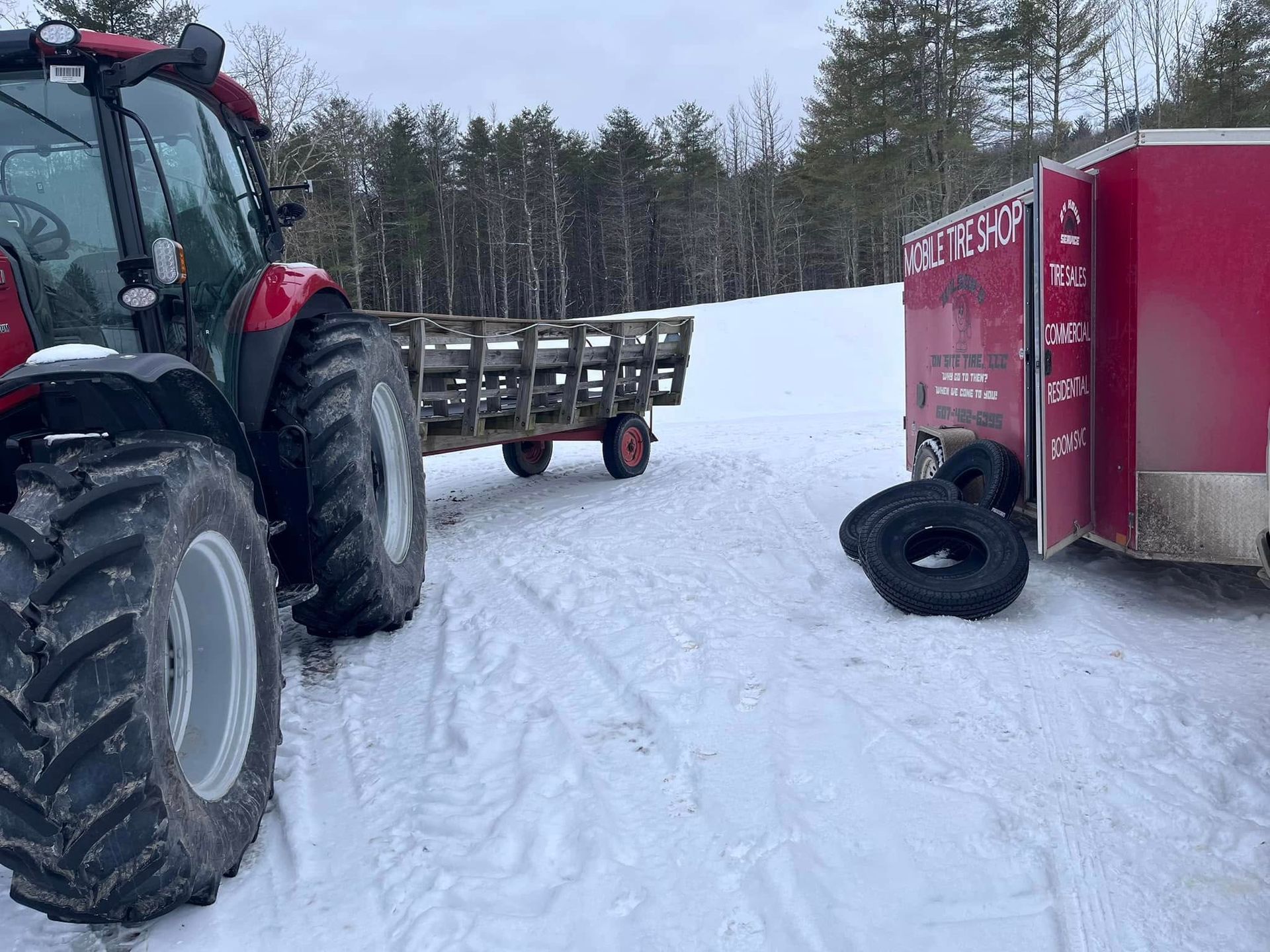 A tractor is pulling a trailer full of tires in the snow.