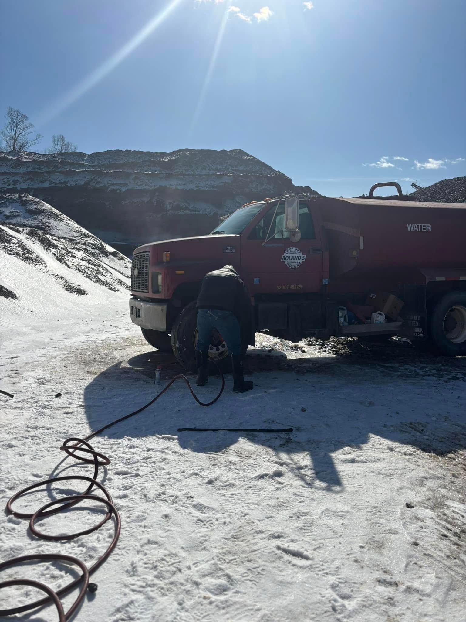 A man is working on a red truck in the snow.