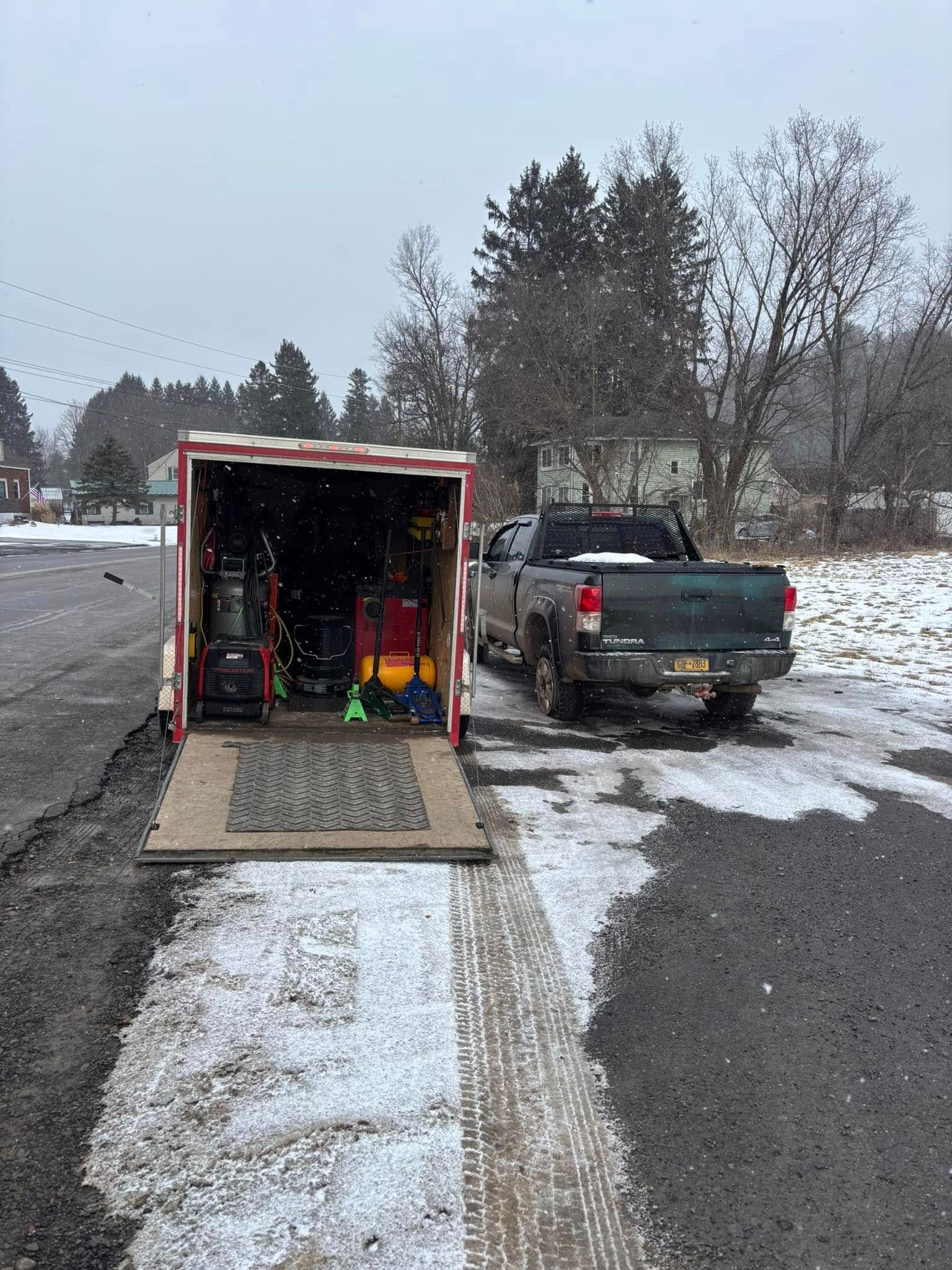 A truck is being towed by a trailer on a snowy road.