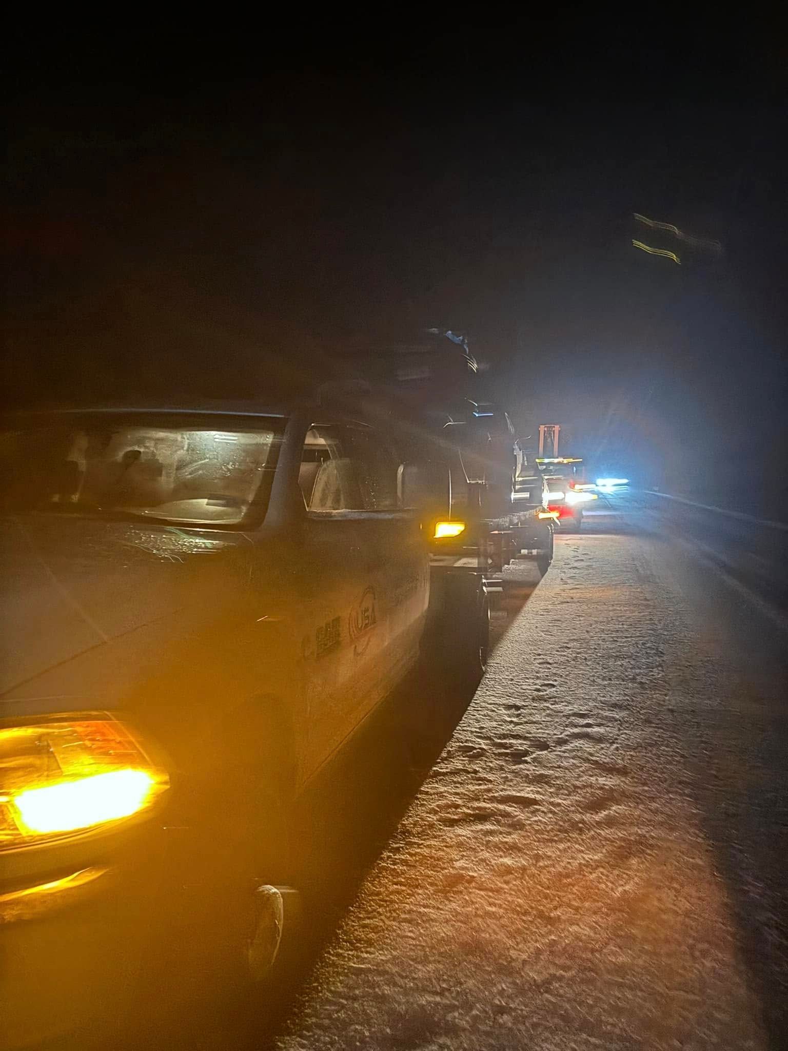 A row of cars are parked on the side of a road at night.