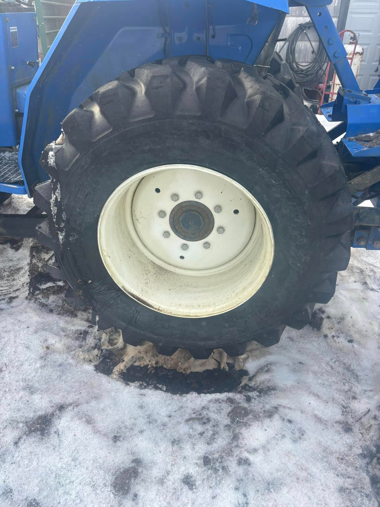 A close up of a tire on a blue tractor in the snow.