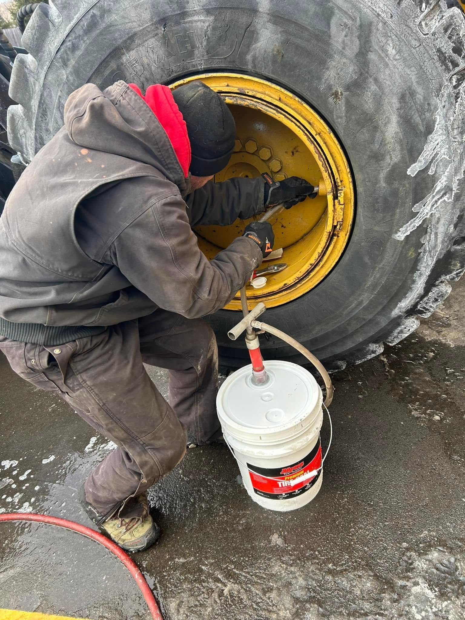 A man is cleaning a tire with a hose next to a bucket of oil.
