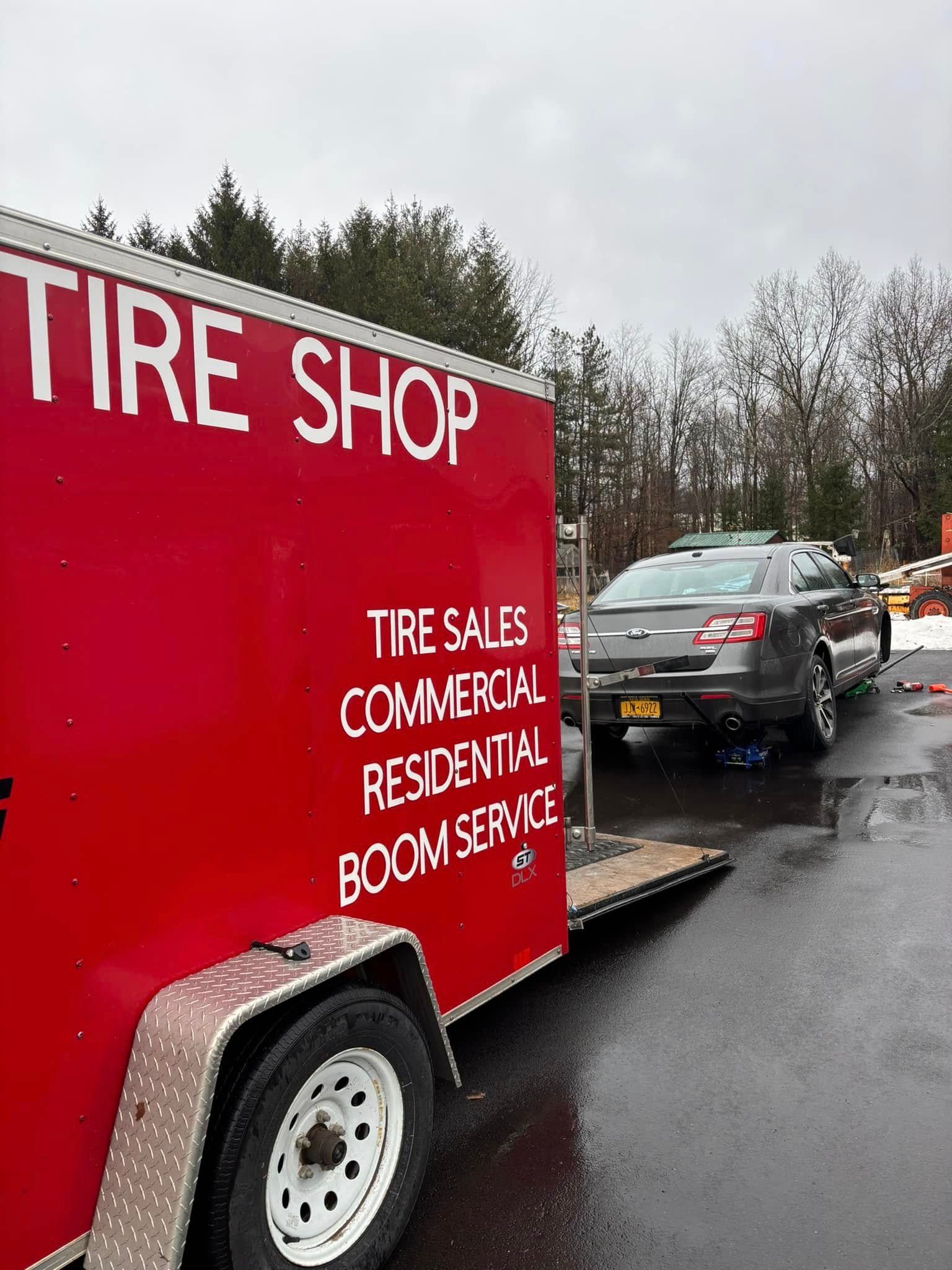A red tire shop trailer is being towed by a car.