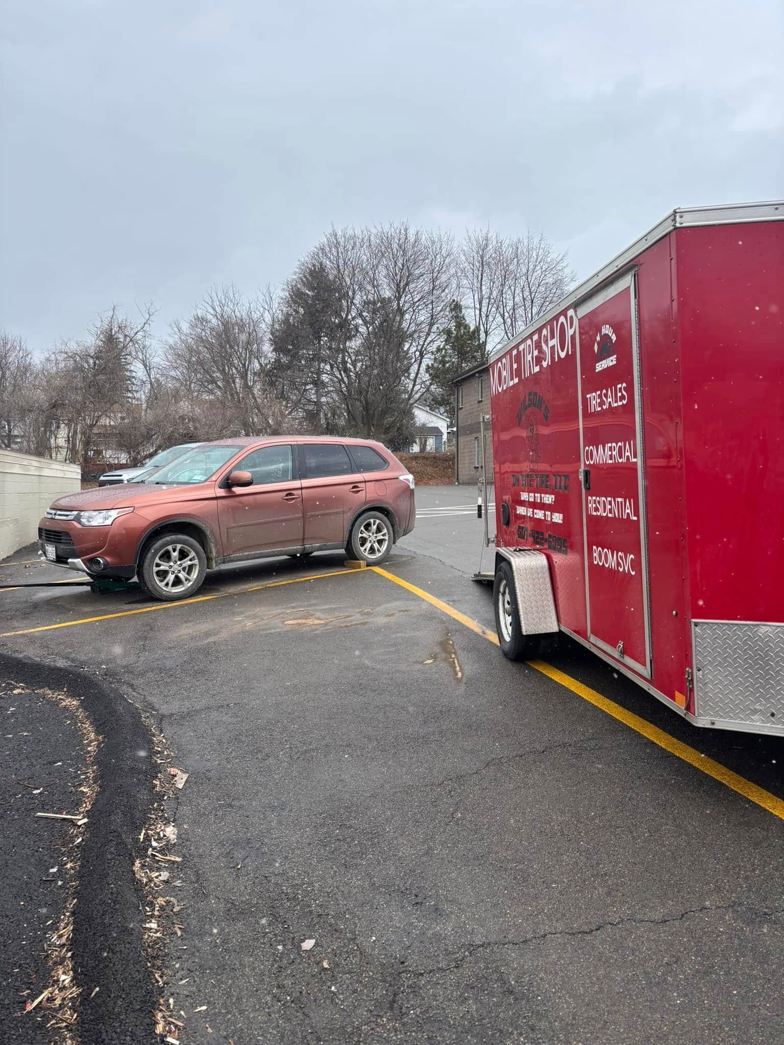 A red car is parked next to a red trailer in a parking lot.