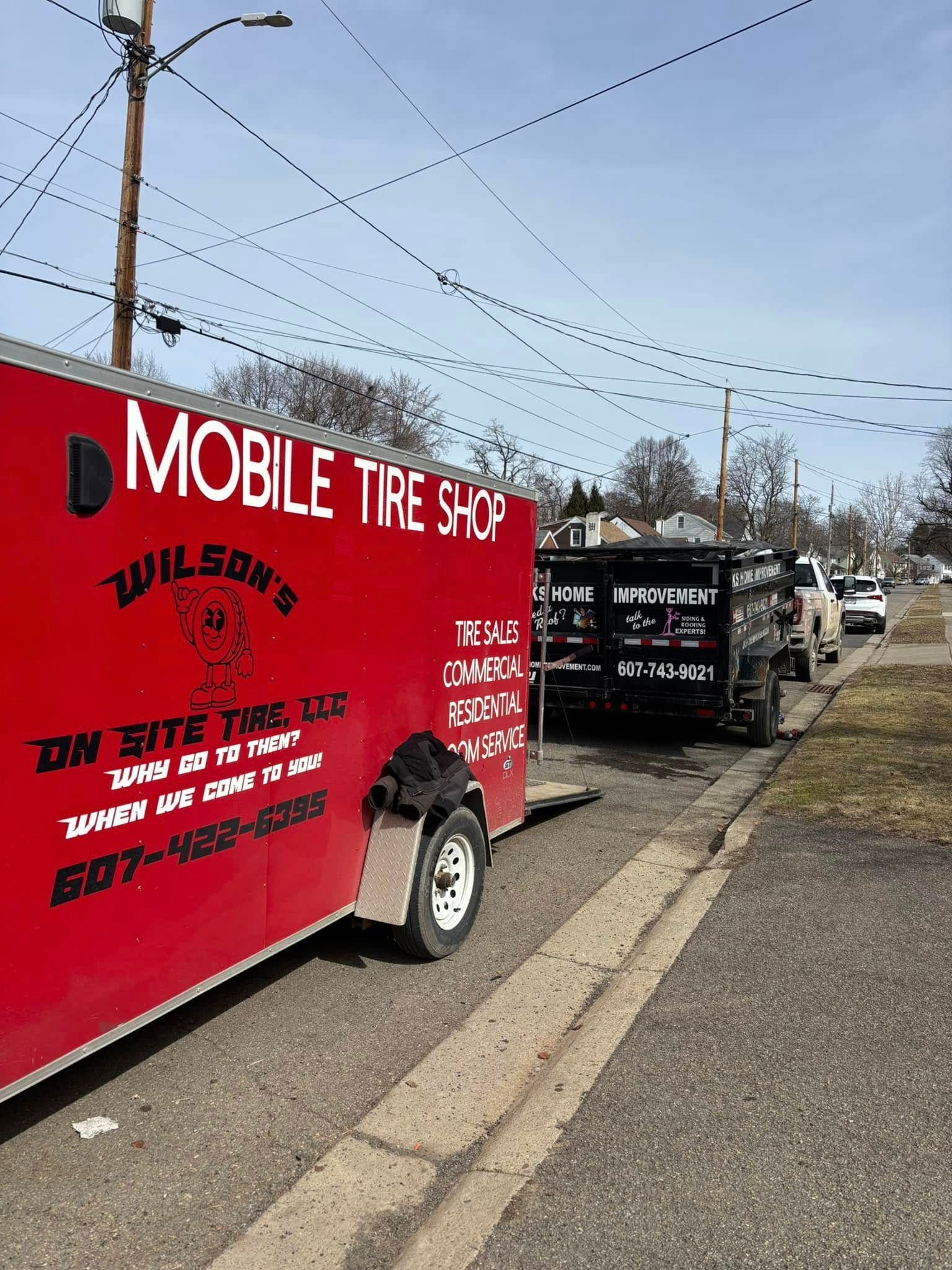 A red mobile tire shop trailer is parked on the side of the road.