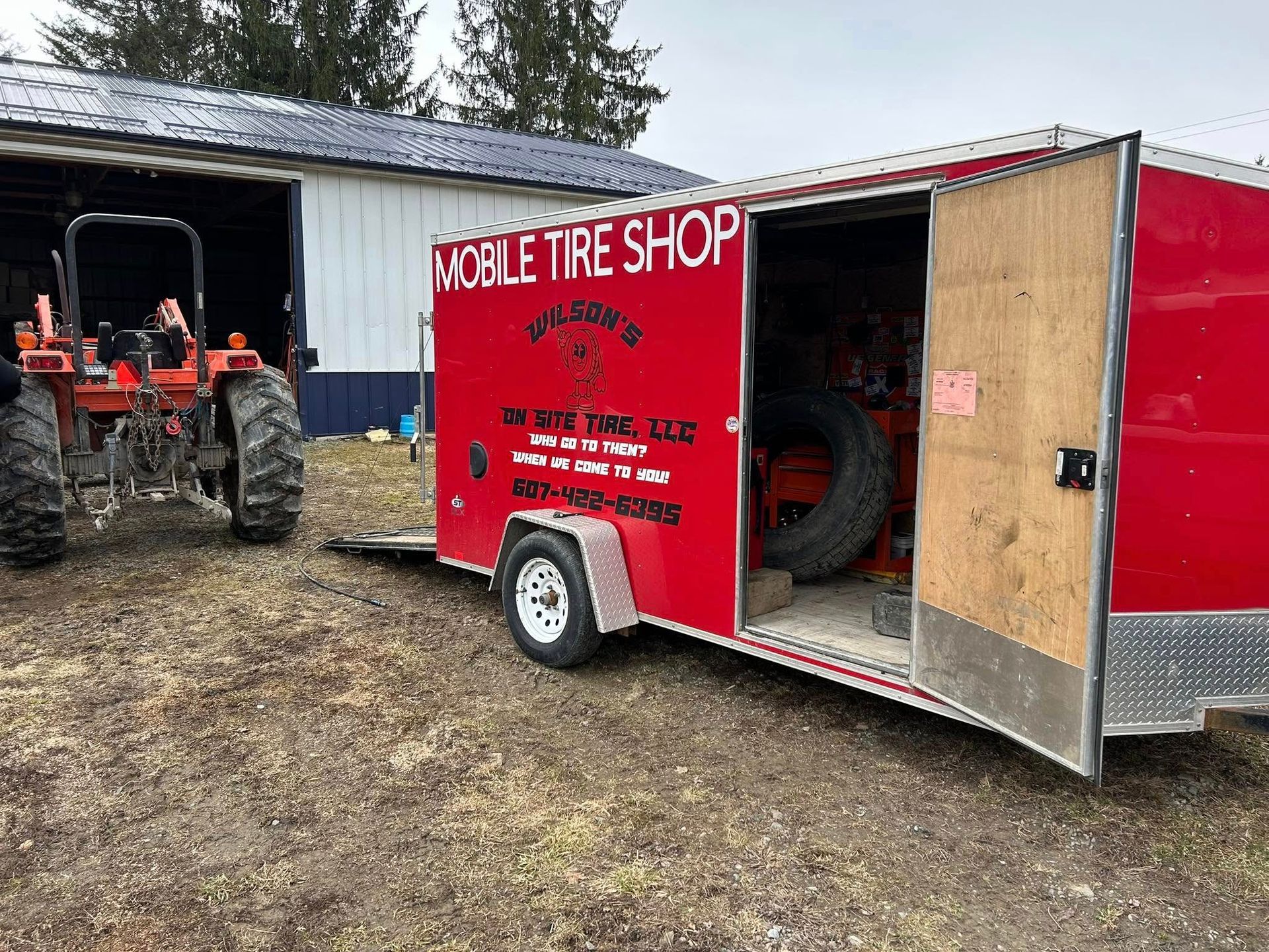 A red trailer with a tire inside of it is parked in front of a tractor.