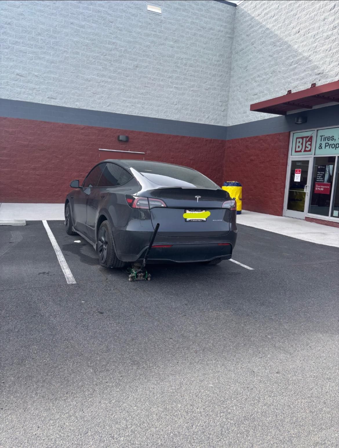 A tesla model 3 is parked in a parking lot in front of a store.