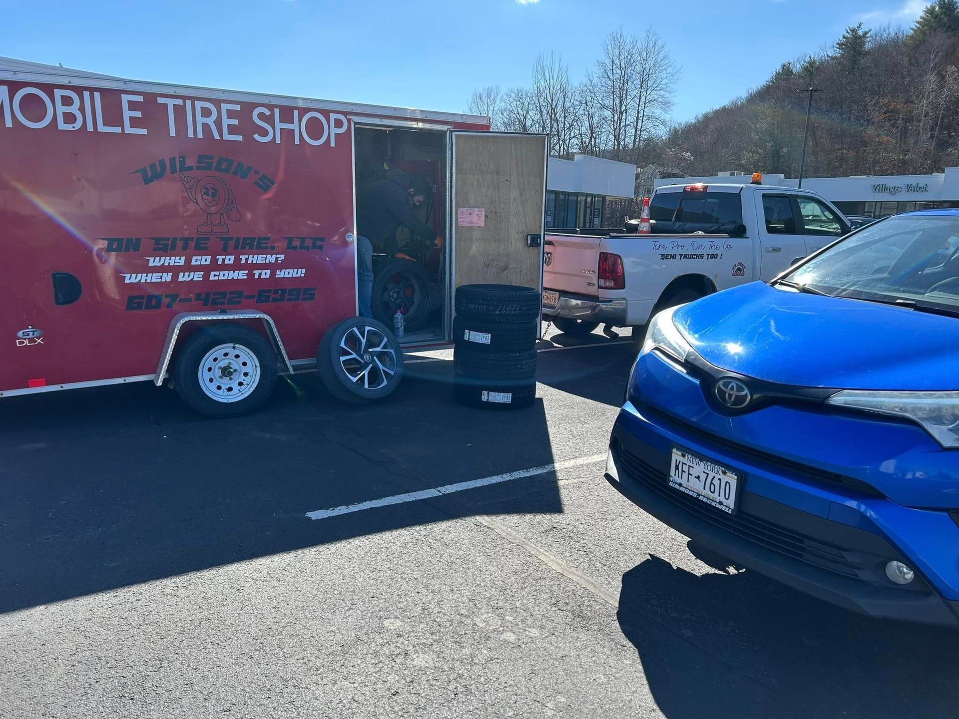 A blue car is parked in front of a mobile tire shop trailer