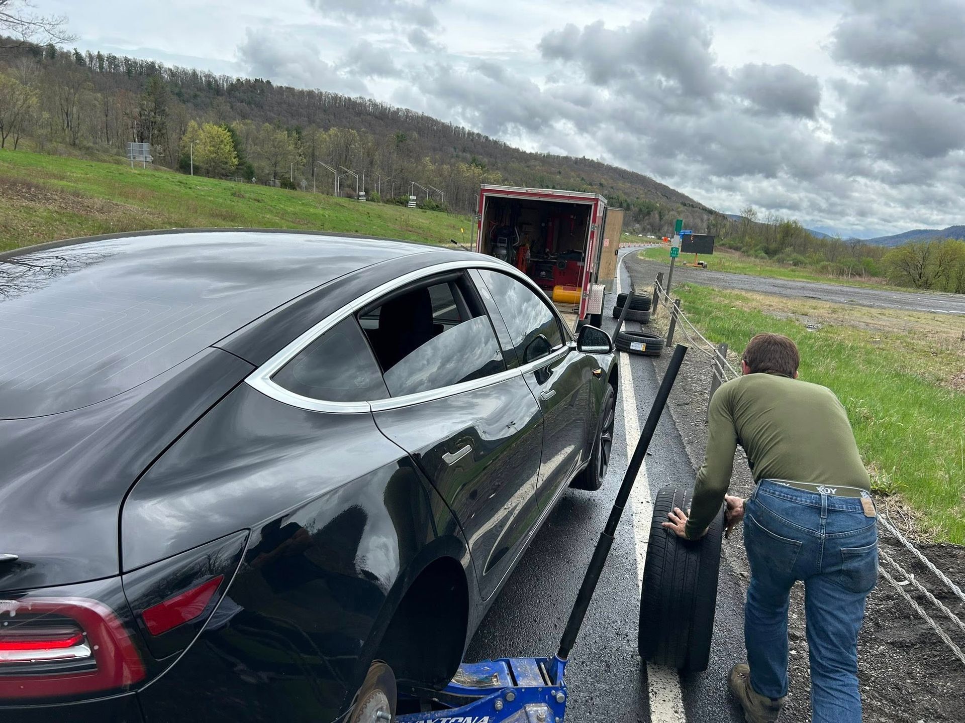 A man is pushing a black car on a tow truck.