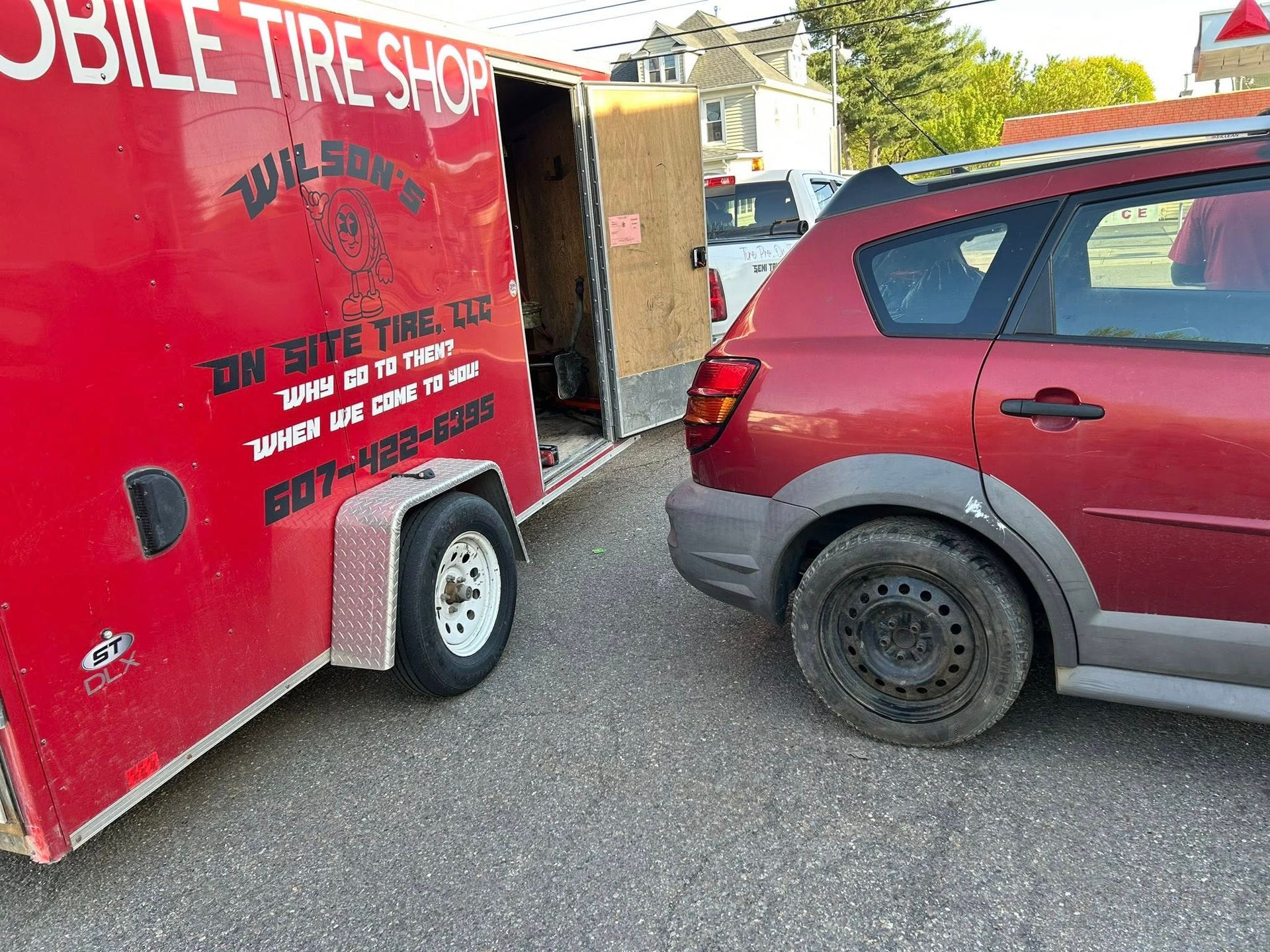 A red car is parked next to a trailer that says mobile tire shop