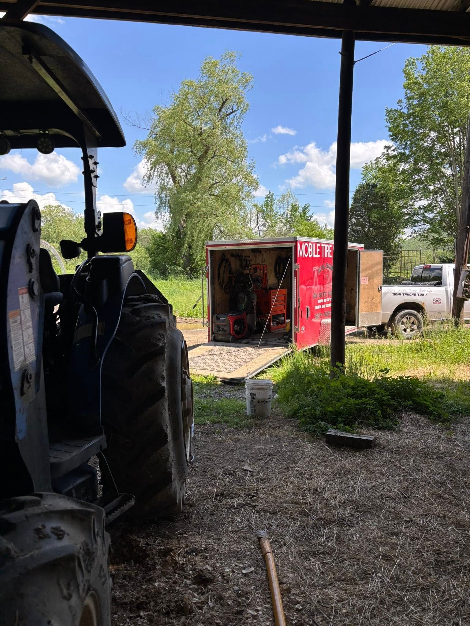 A tractor is parked under a shed next to a trailer.
