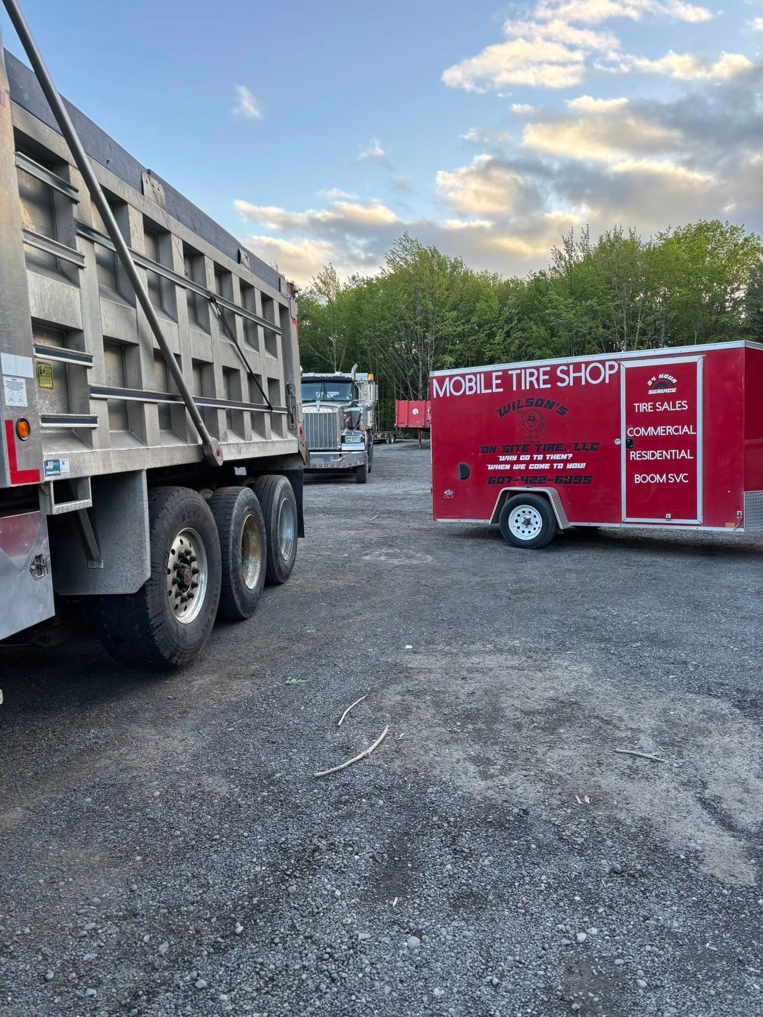 A dump truck is parked next to a red trailer in a gravel lot.