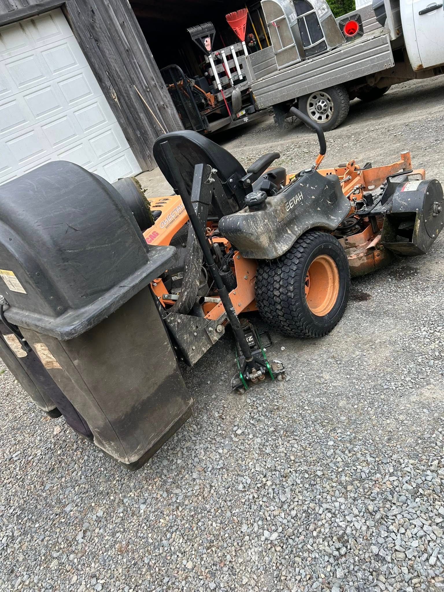 A lawn mower is sitting in a gravel lot next to a truck.