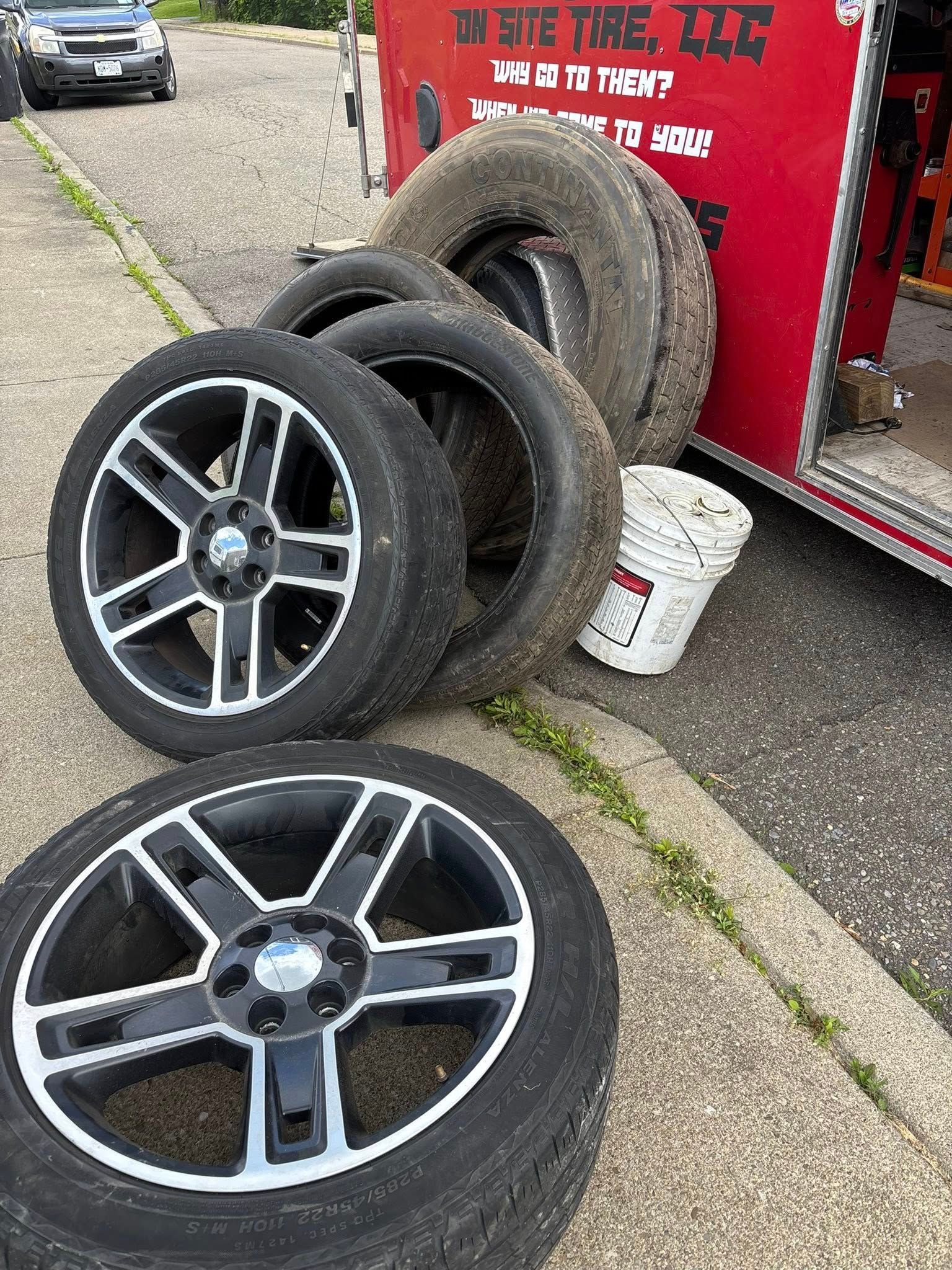 A pile of tires and wheels are sitting on the sidewalk next to a red truck.
