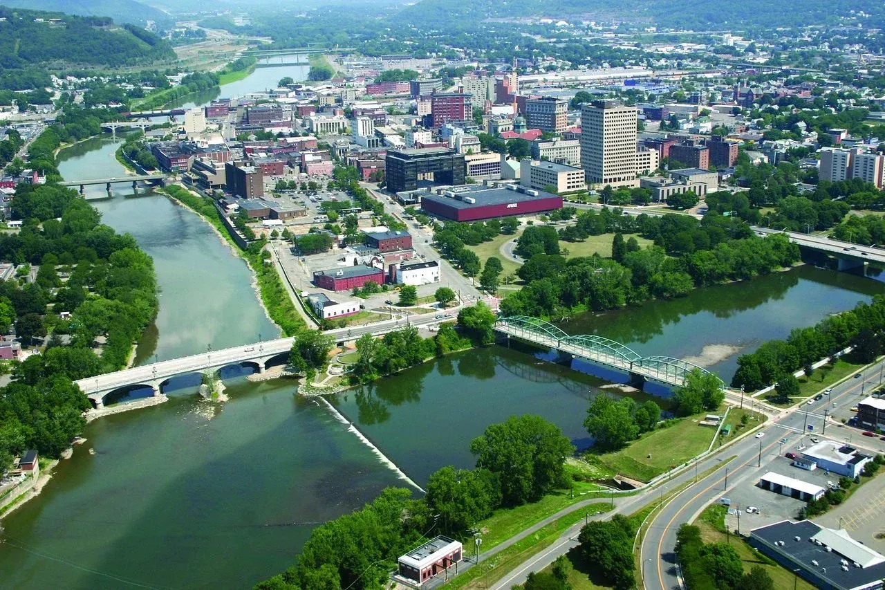 Aerial view of a city with bridges over a river; several buildings and green trees are visible.
