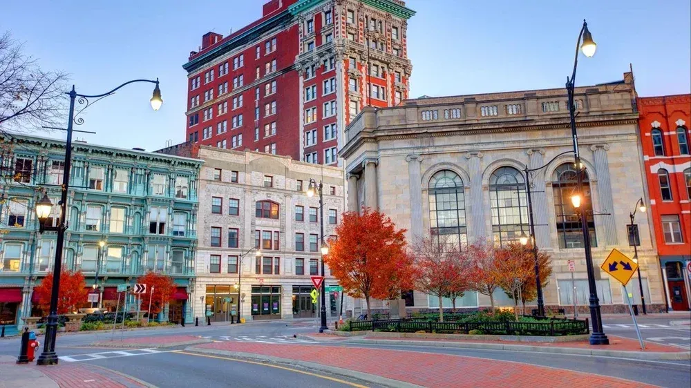 Downtown street scene with buildings in various architectural styles, autumn trees, and streetlights.
