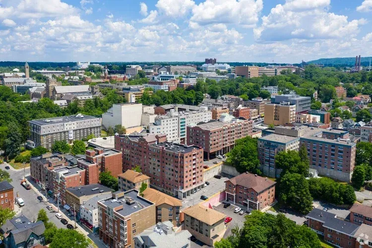 Aerial view of a city with brick buildings, trees, and blue sky with clouds.