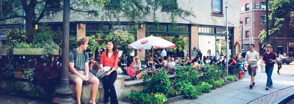 People enjoying a sunny day outdoors: sitting at a cafe with an umbrella and walking along a sidewalk.