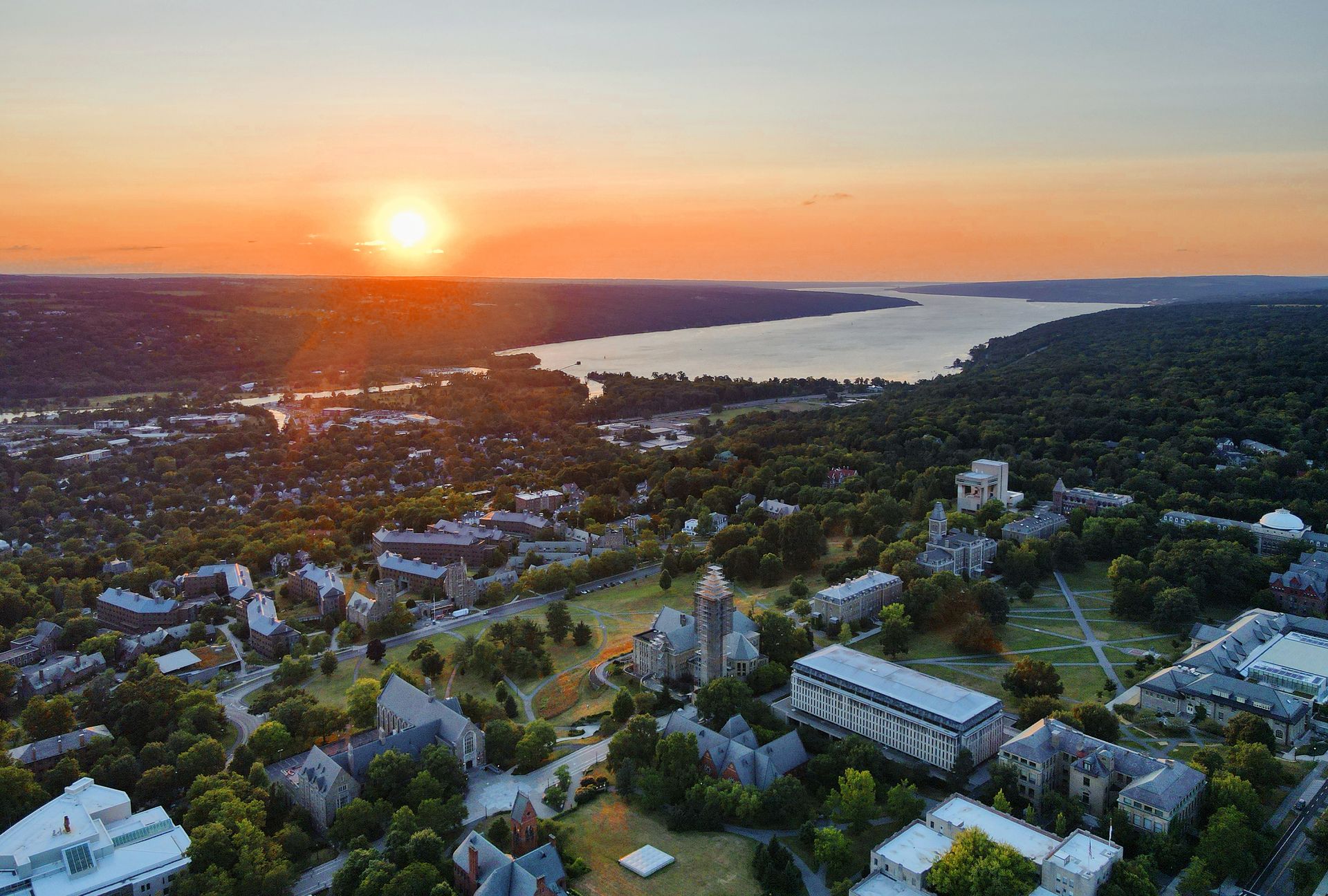 Aerial view of a campus at sunset with a lake in the background and a warm orange sky.
