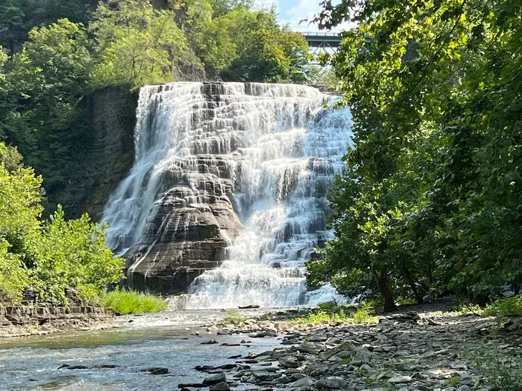 Waterfall cascading down layered rock, surrounded by green trees and foliage.