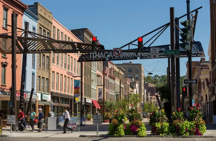 View of Ithaca Commons street with shops, pedestrians, and decorative archway under a clear blue sky.