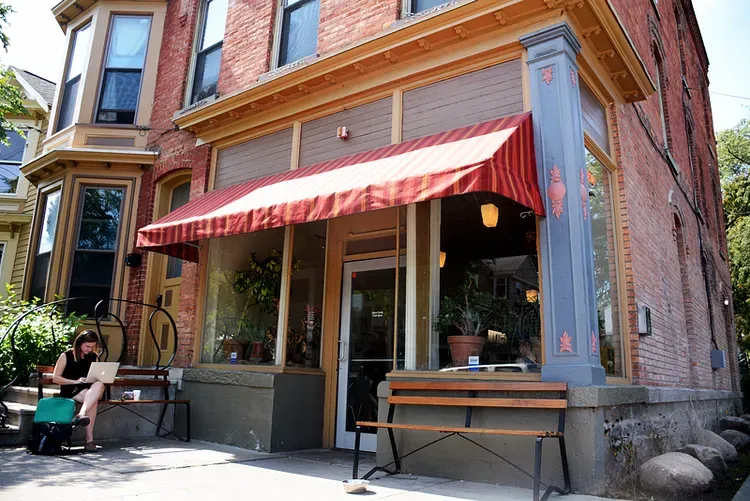 Cafe exterior with red awning, person working on a laptop on the bench outside.