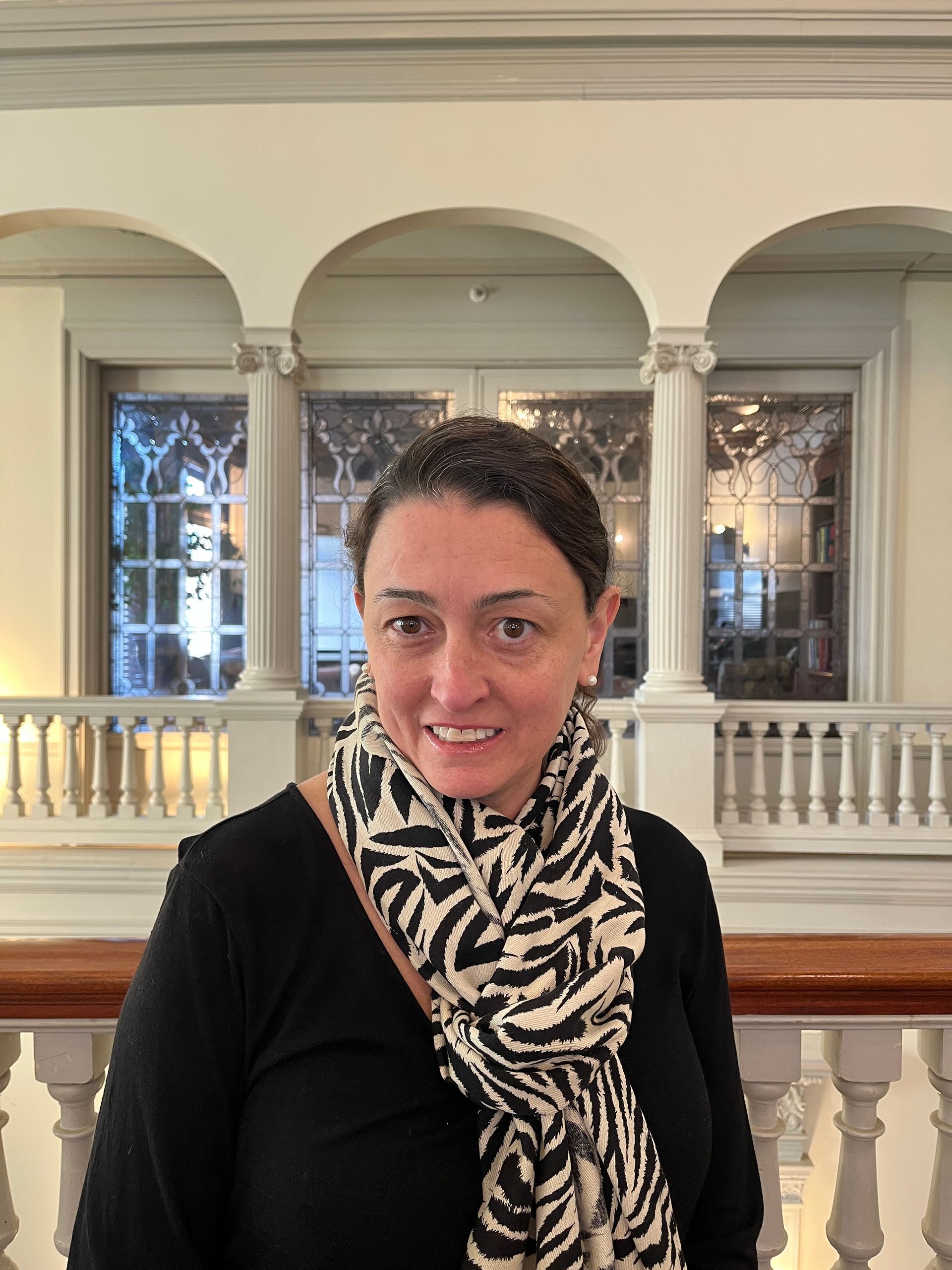 Woman with black and white scarf smiles in a room with arched windows.