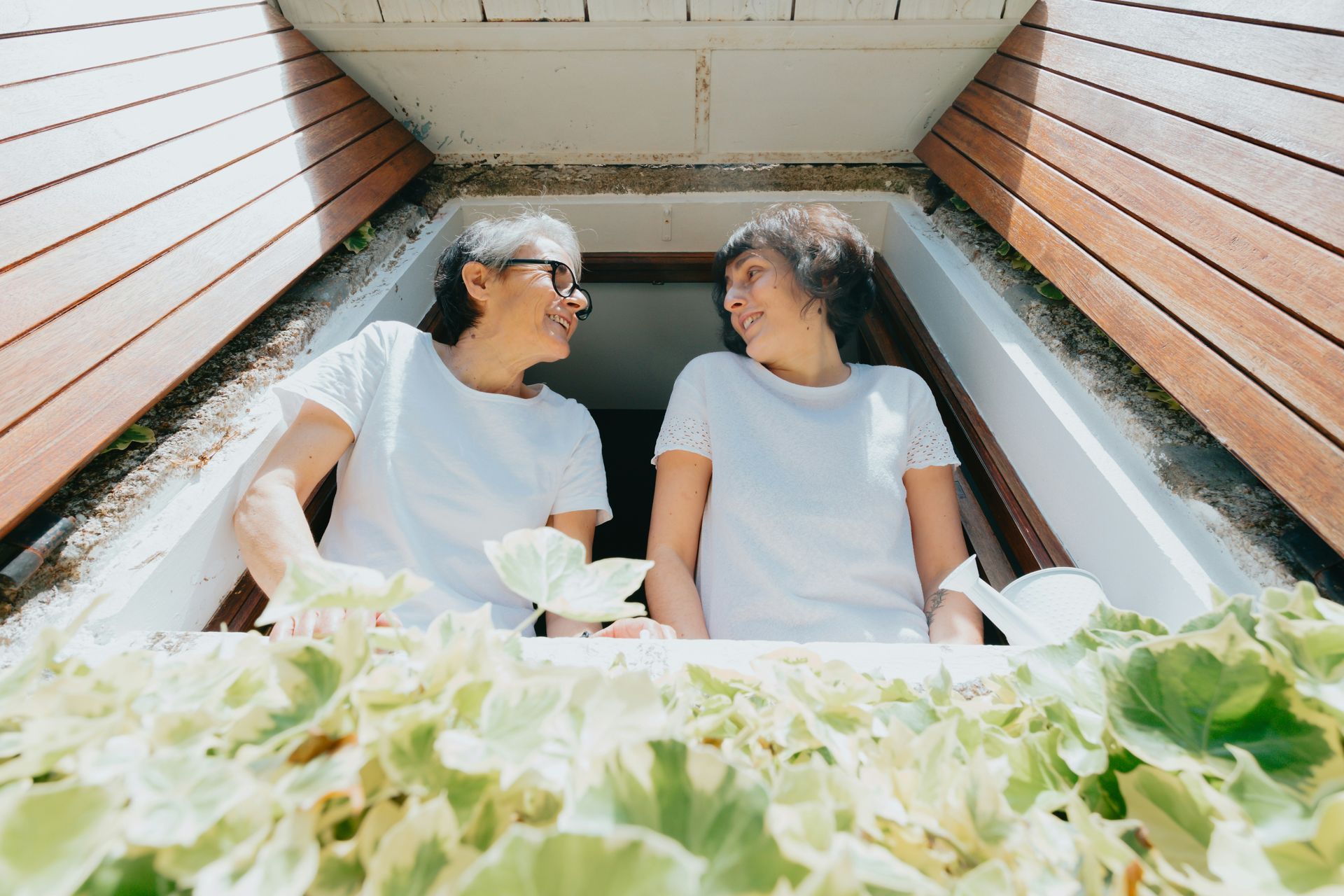 Two older women are looking out of a window.