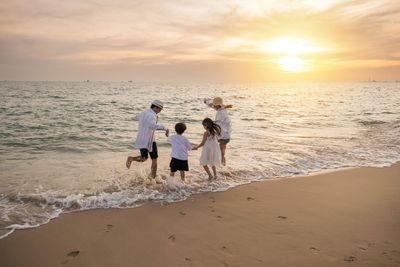 Family walking along a sandy beach at sunset, with waves washing onto the shore.