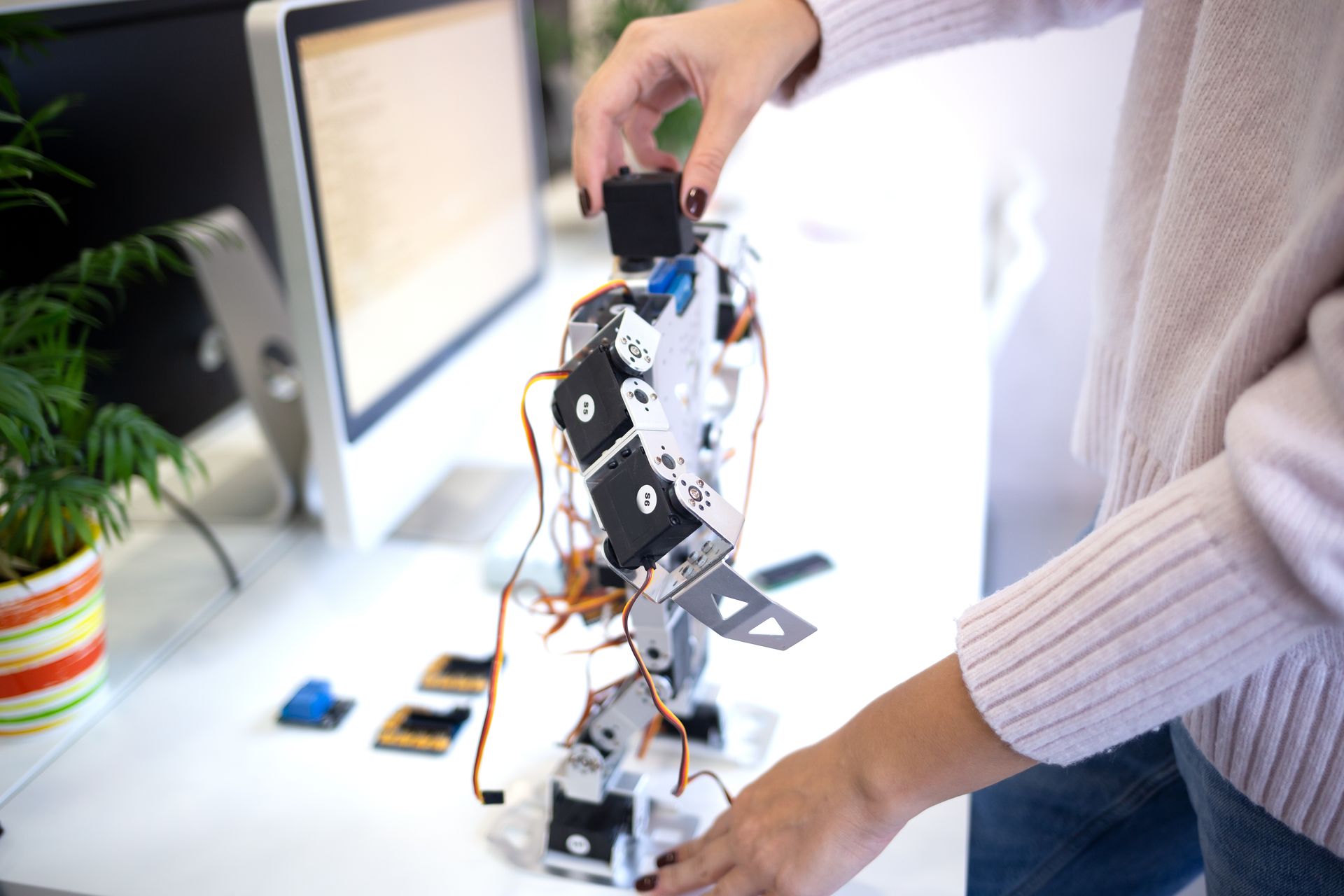 A woman is working on a robot in front of a computer.