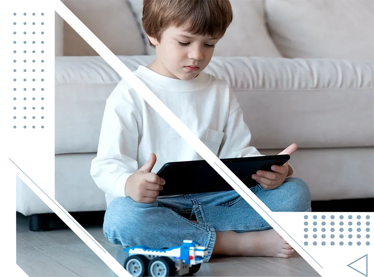 A young boy is sitting on the floor playing with a tablet.