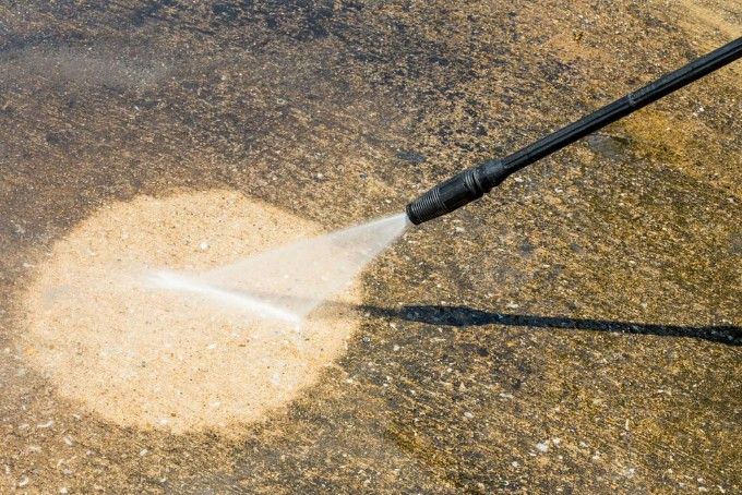 A Person is Using a High Pressure Washer to Clean a Concrete Floor — Hire Power NT in Berrimah, NT