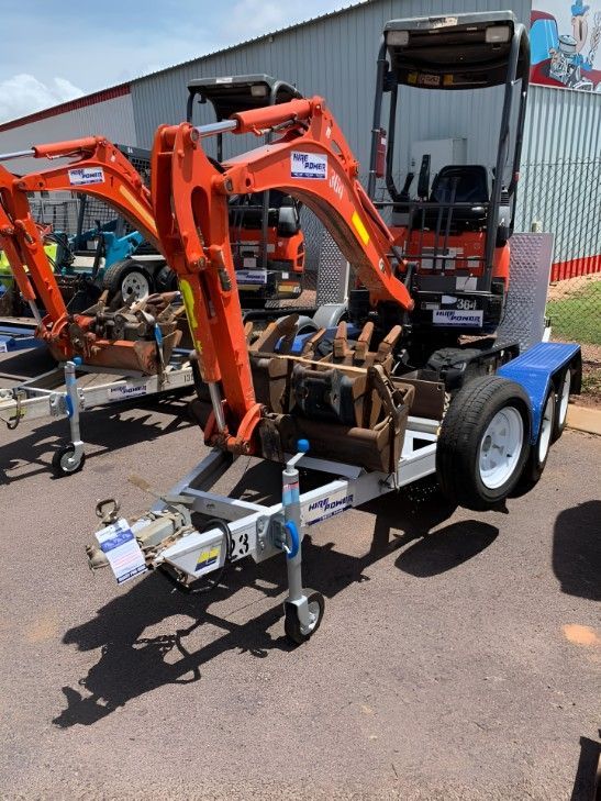 A Trailer With an Excavator on It is Parked in Front of a Building — Hire Power NT in Berrimah, NT