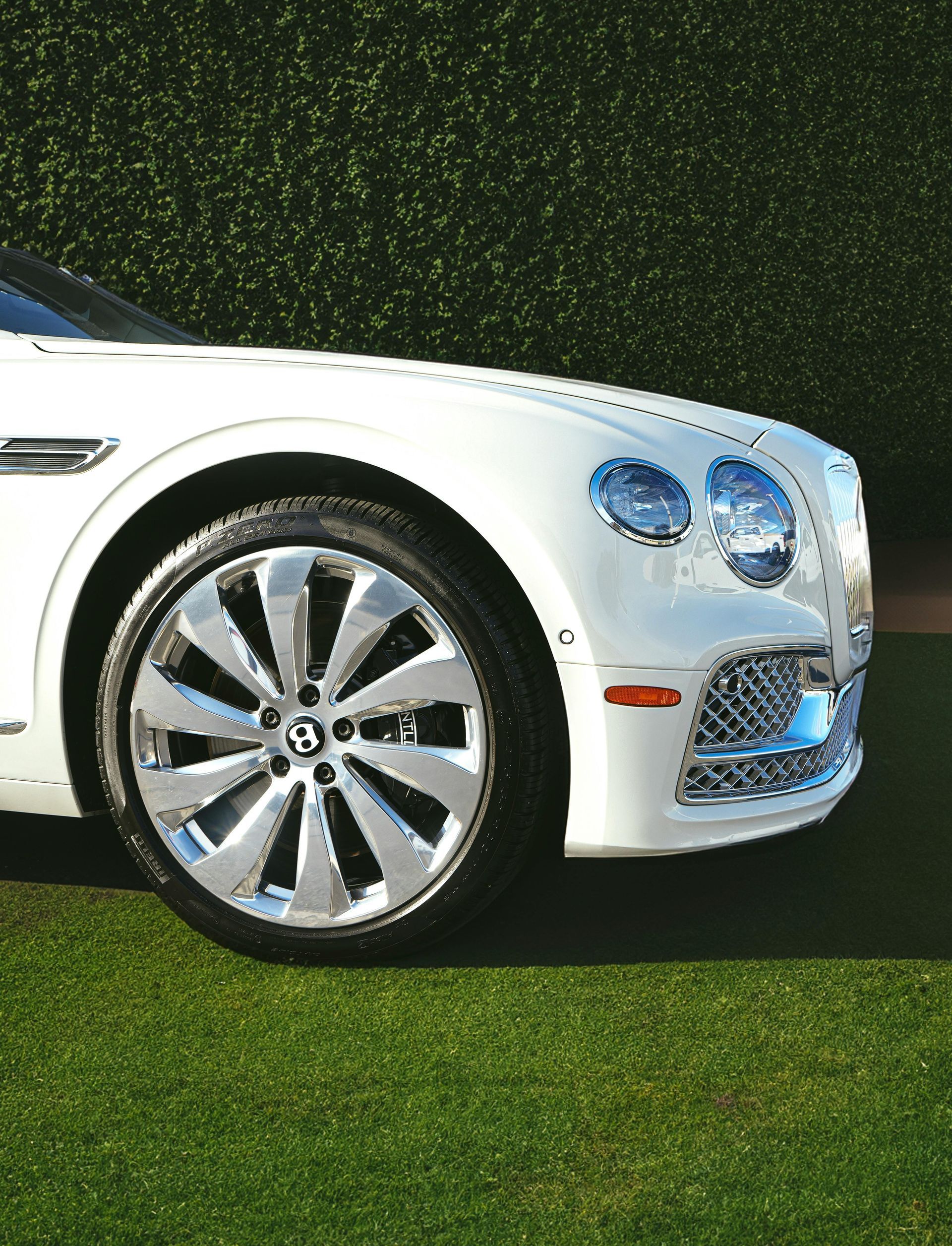 A white bentley is parked on a lush green field.