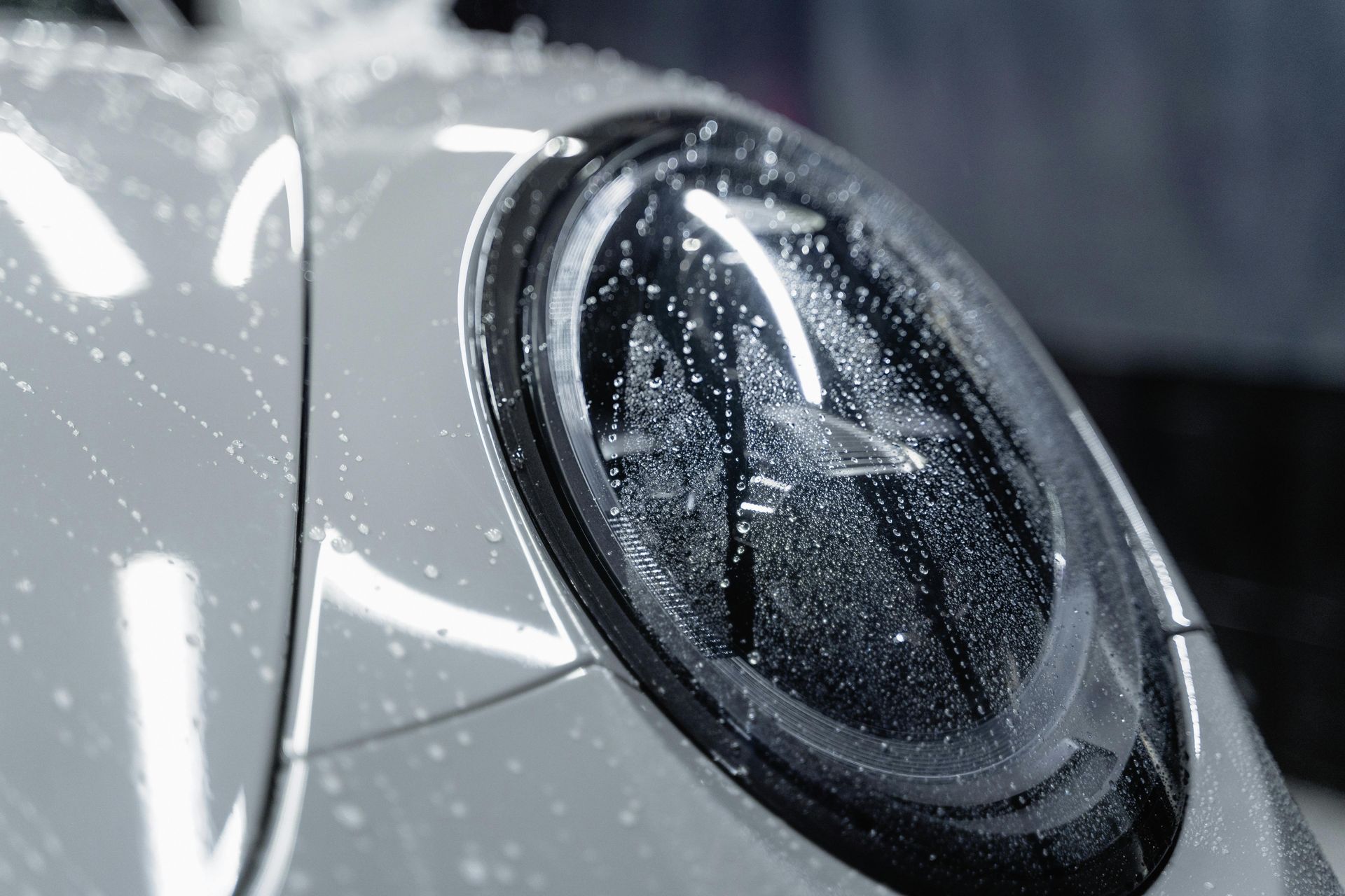 A close up of a car headlight with water drops on it.