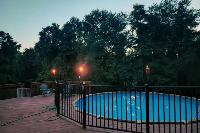 Beautiful aboveground pool with ambience lighting lanterns at dusk. Background of mature forest. Calming and peaceful scene