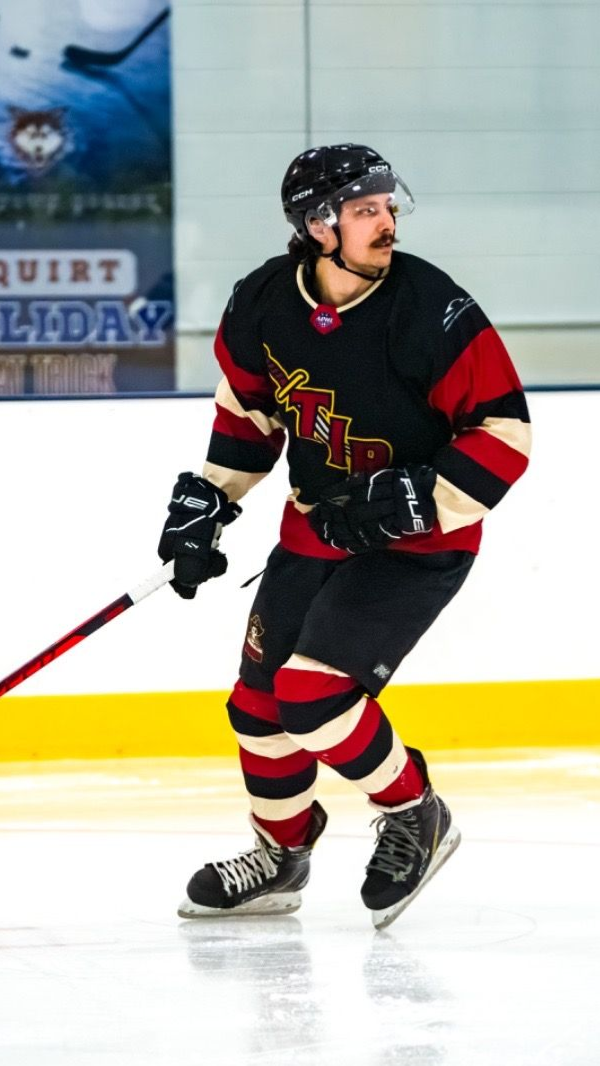A hockey player in a black, red, and cream jersey skating on an ice rink during a game.