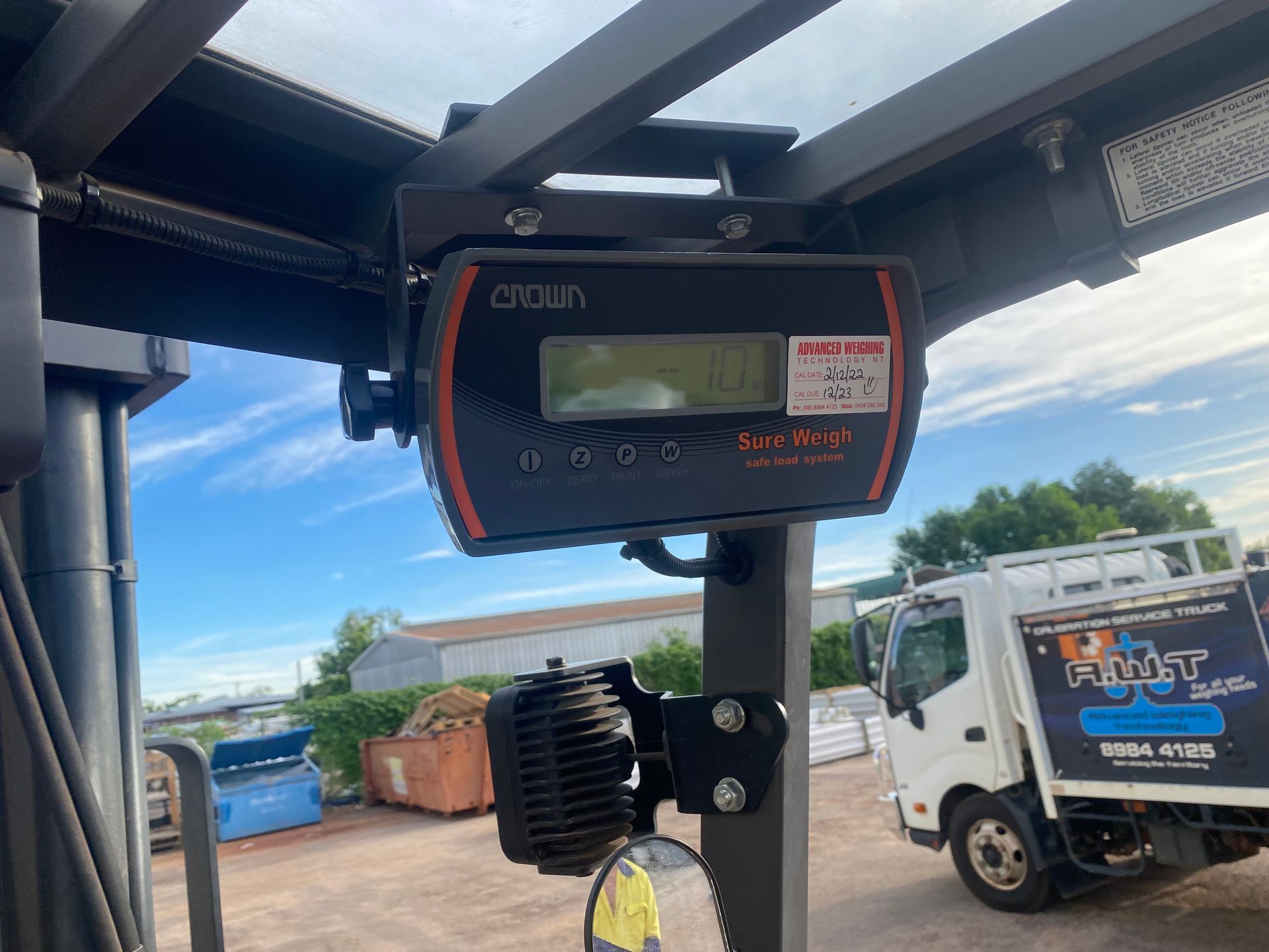 A digital weight scale mounted inside a forklift cabin, with an outdoor view of a truck and industrial yard in the back  — Advanced Weighing Technology NT Pty Ltd In Winnellie, NT