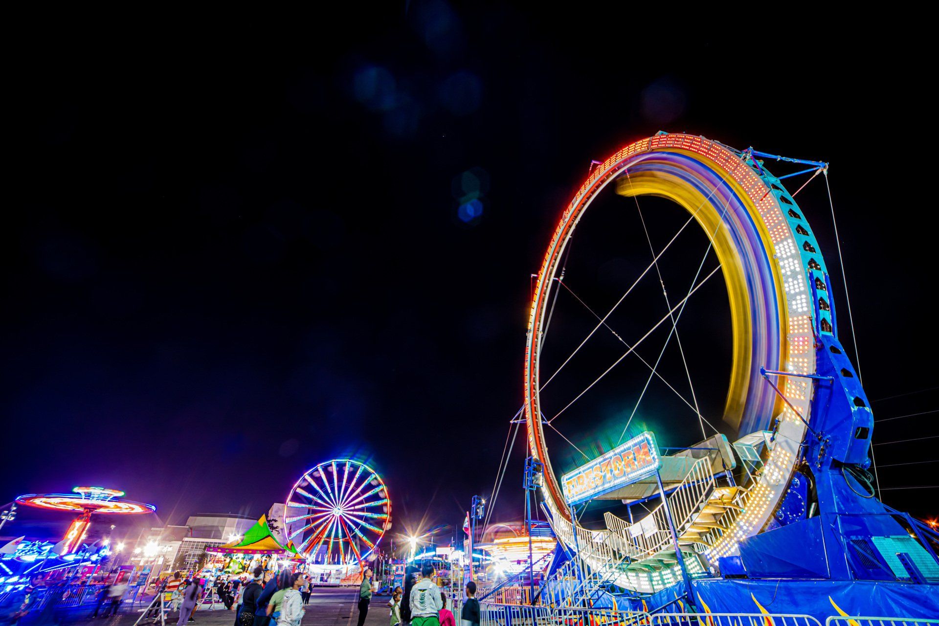 A carnival at night with ferris wheels and a giant ring ride.